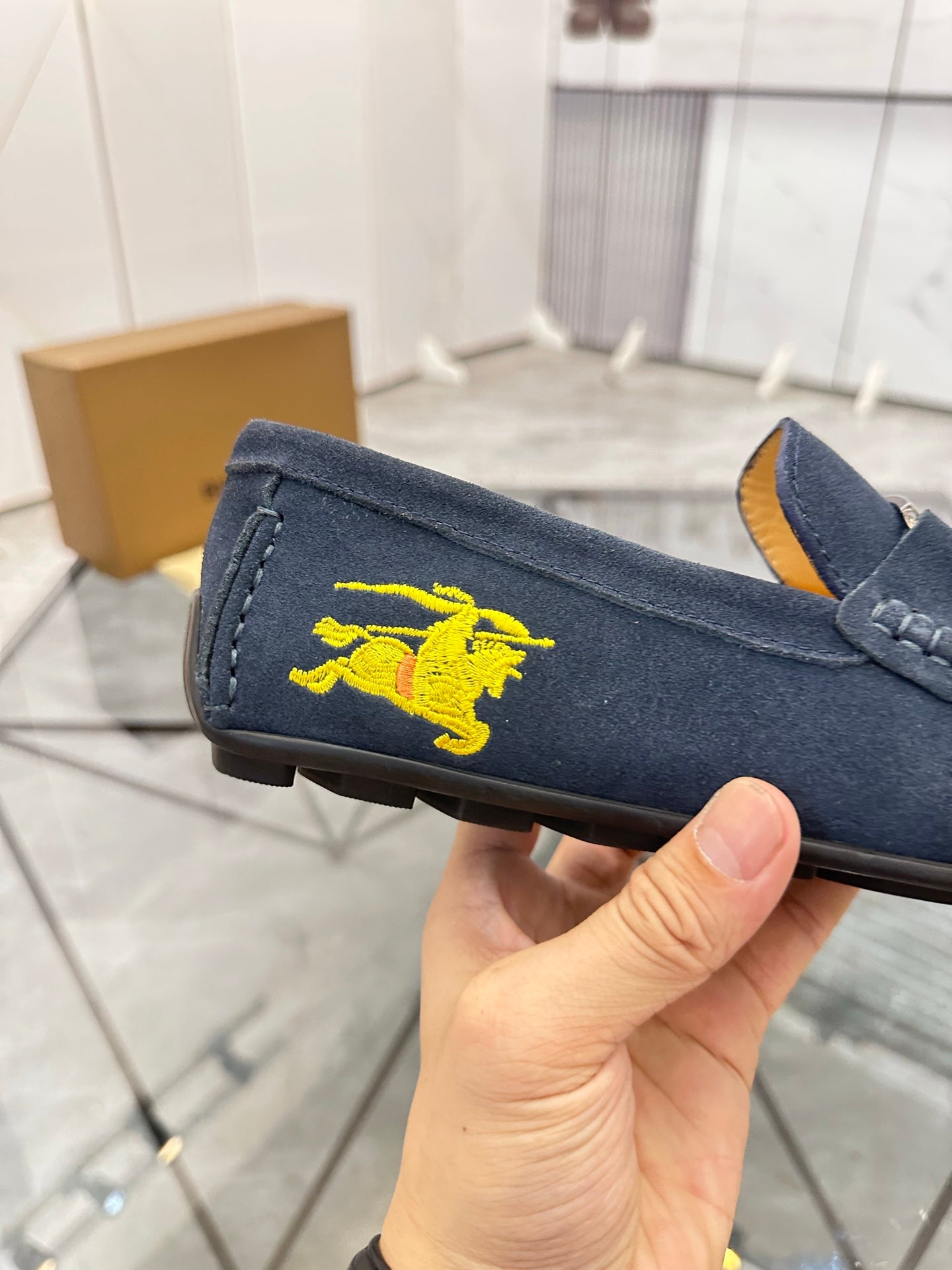Navy suede loafer with yellow horse emblem on side, held near sole