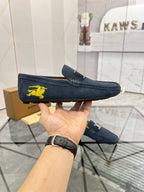 Navy suede loafer in hand, side view with yellow horse emblem