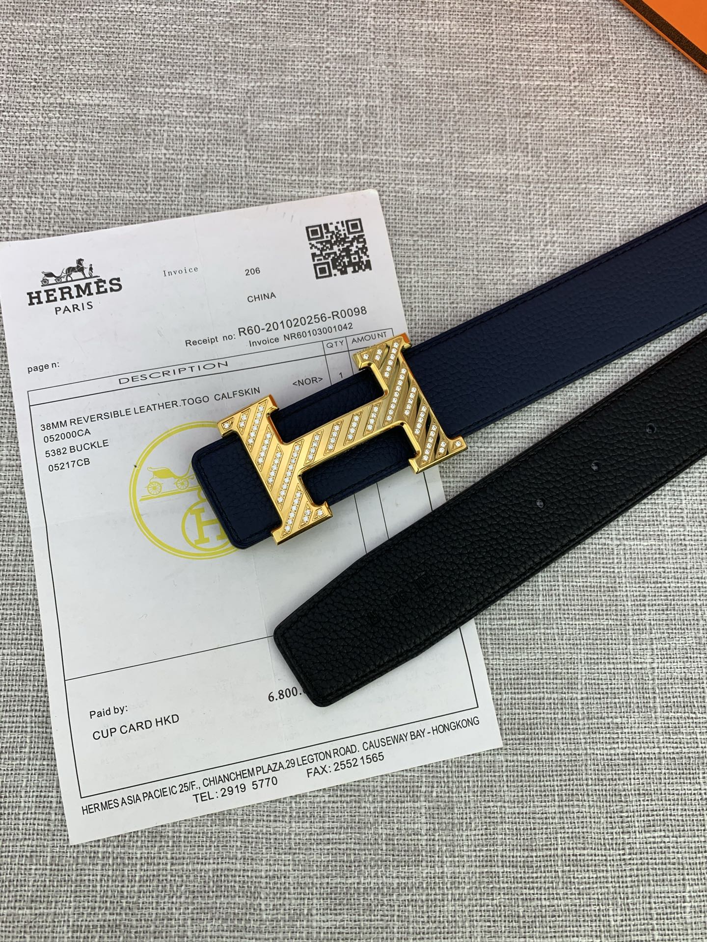 Hermes belt and gold-tone H buckle on packaging paper, shown with dark blue strap