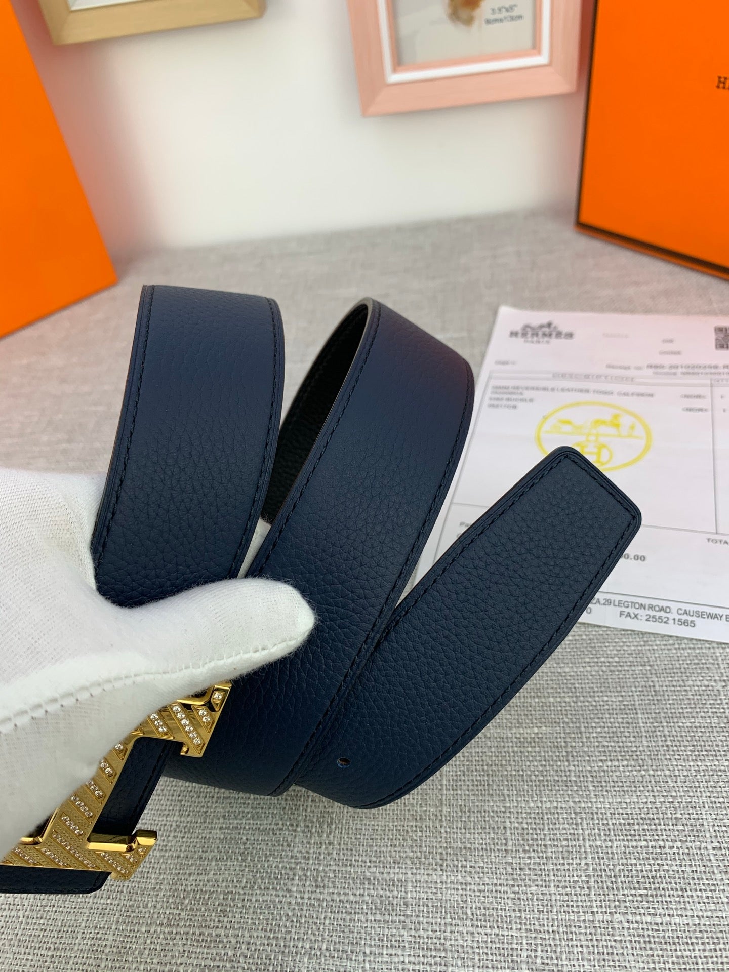 Hermes belt in dark blue with gold-tone buckle detail, straps held by white glove