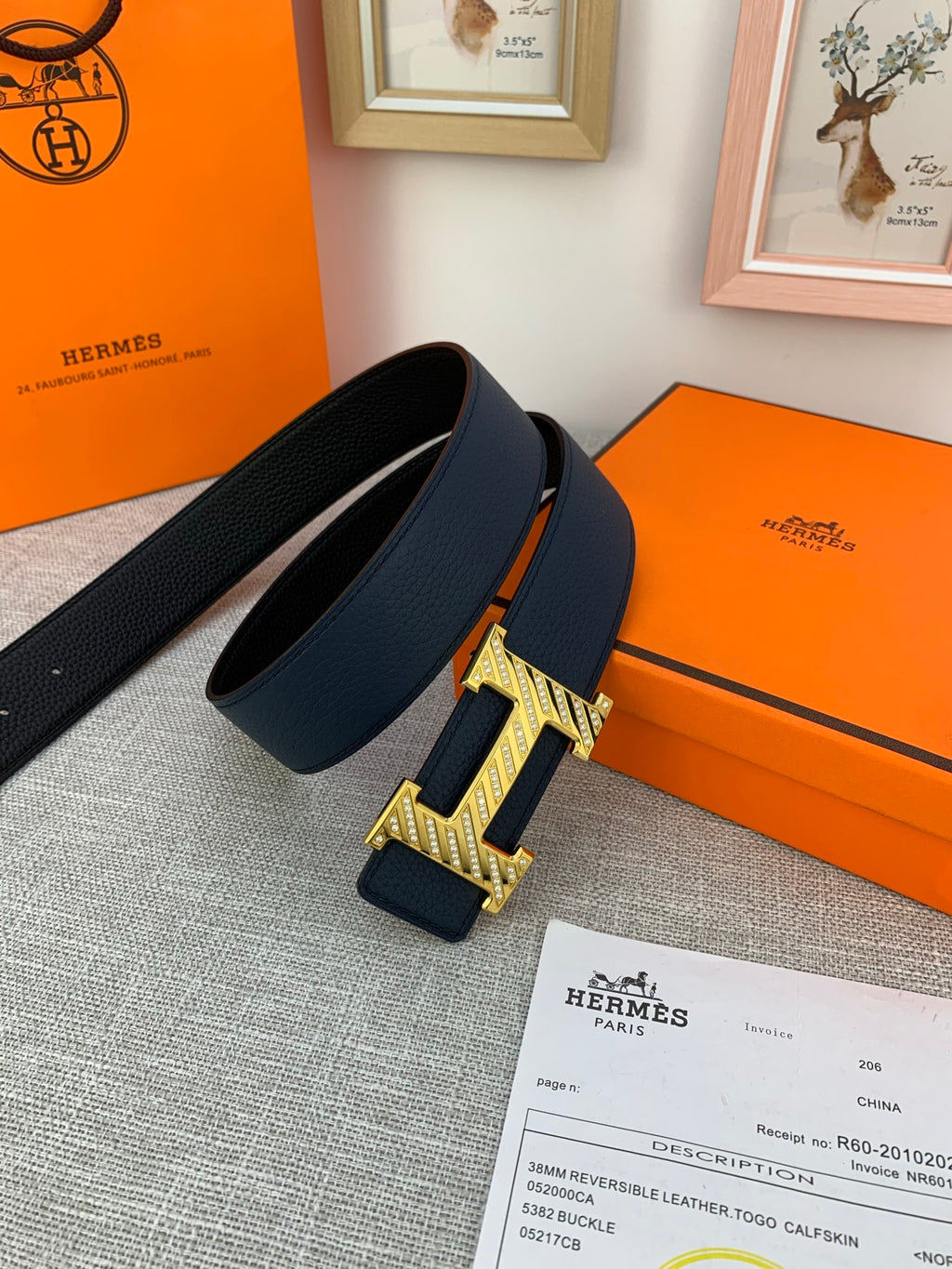 Hermes belt in dark blue with gold-tone buckle, placed beside orange box and papers