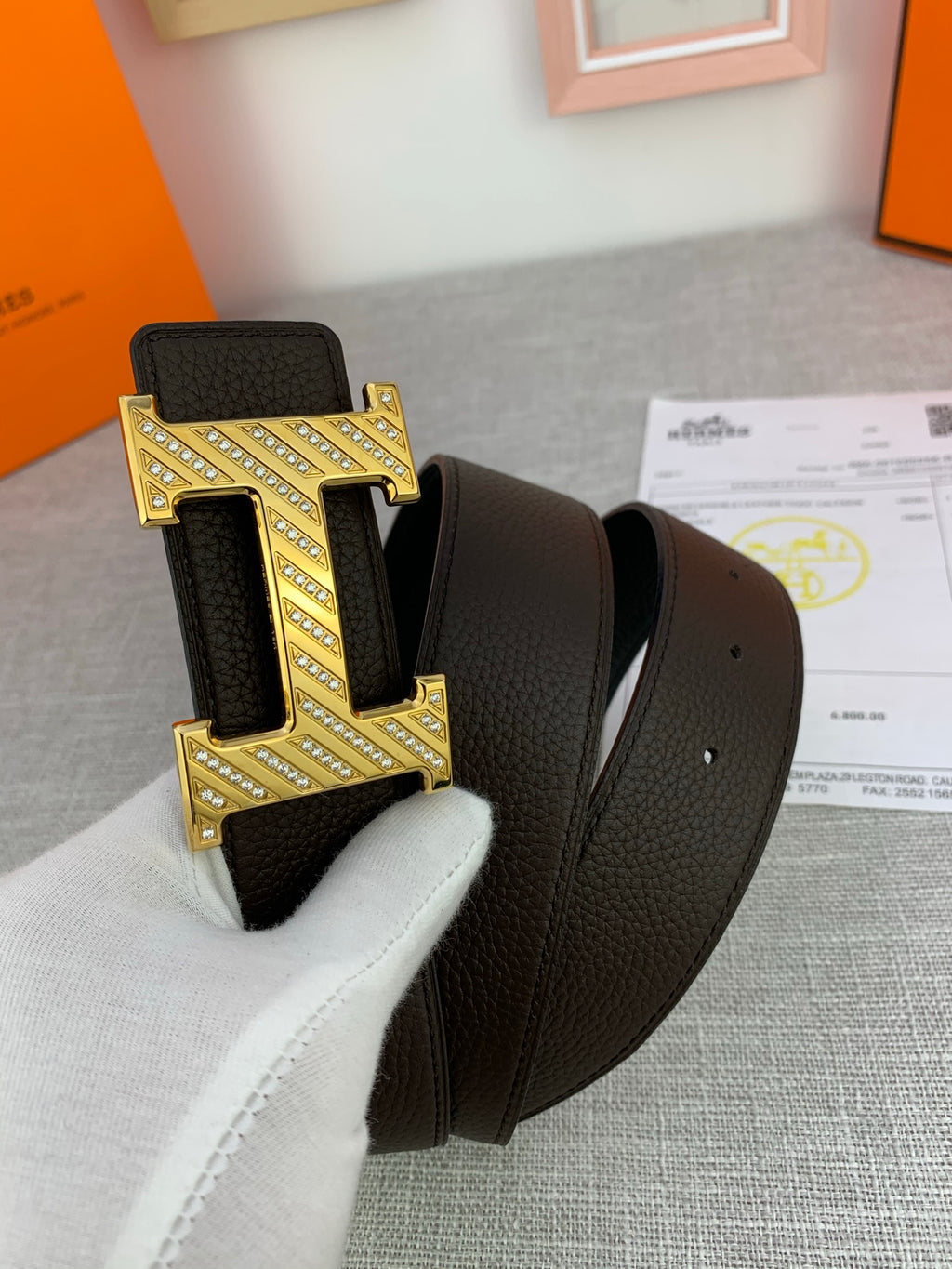 Hermes belt close-up: dark leather and large gold buckle with engraved details