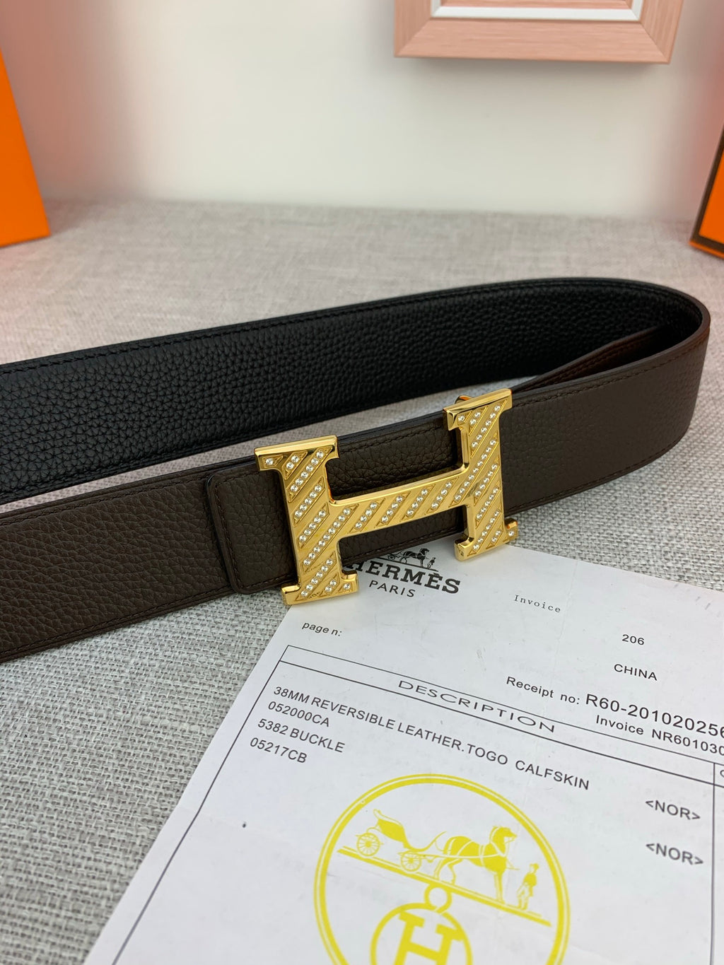 Hermes belt with dark leather strap and gold H buckle, shown with paperwork