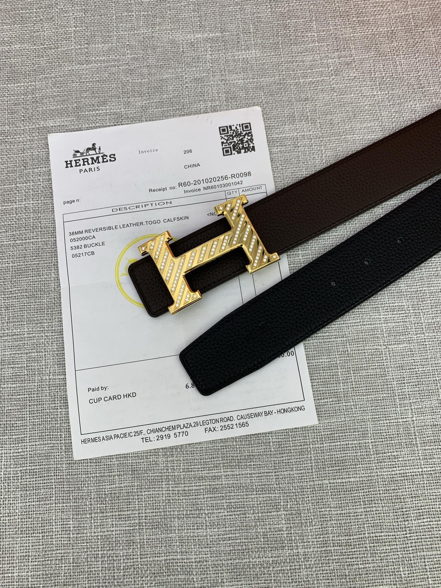 Hermes belt with gold H buckle and dark leather strap beside product paperwork