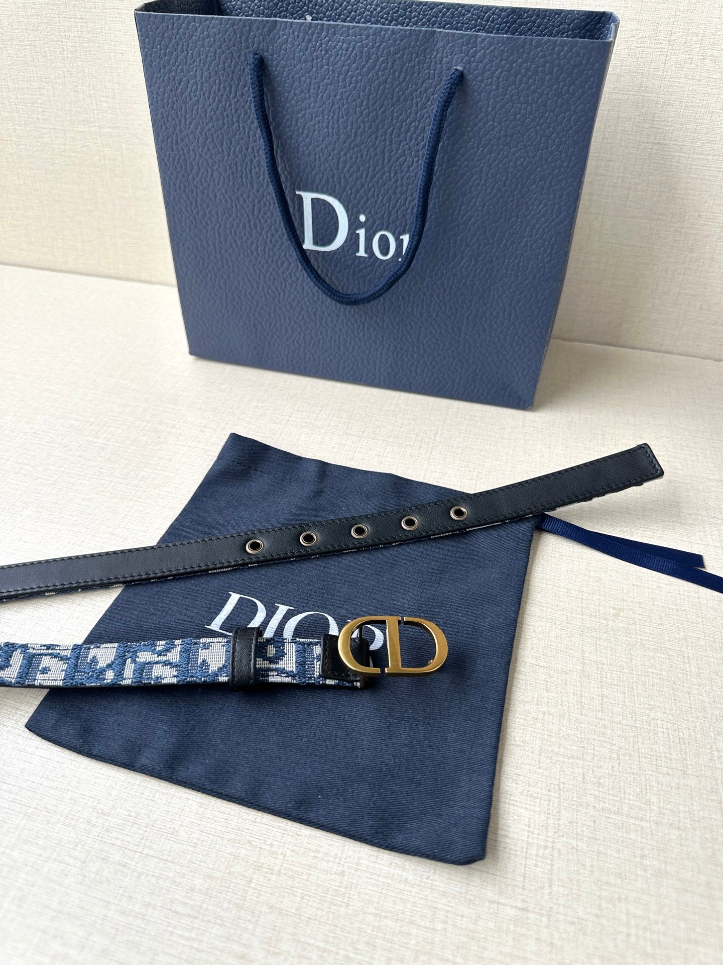 Dior belt laid flat: blue logo strap with gold buckle and black leather keeper