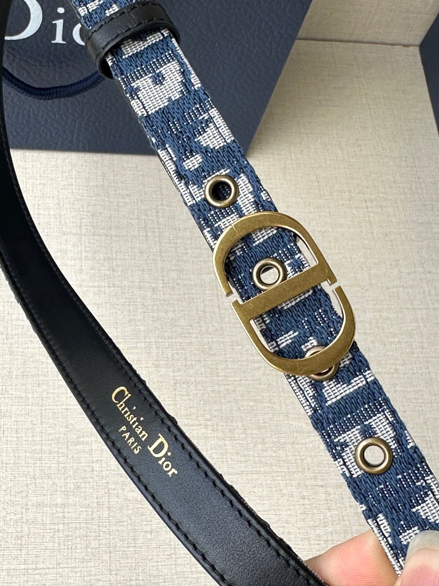 Dior belt close-up: blue logo strap with gold oval buckle and metal eyelets