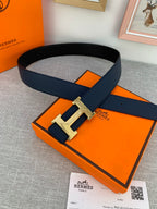 Hermes belt with dark navy strap and gold-tone H buckle, styled on box