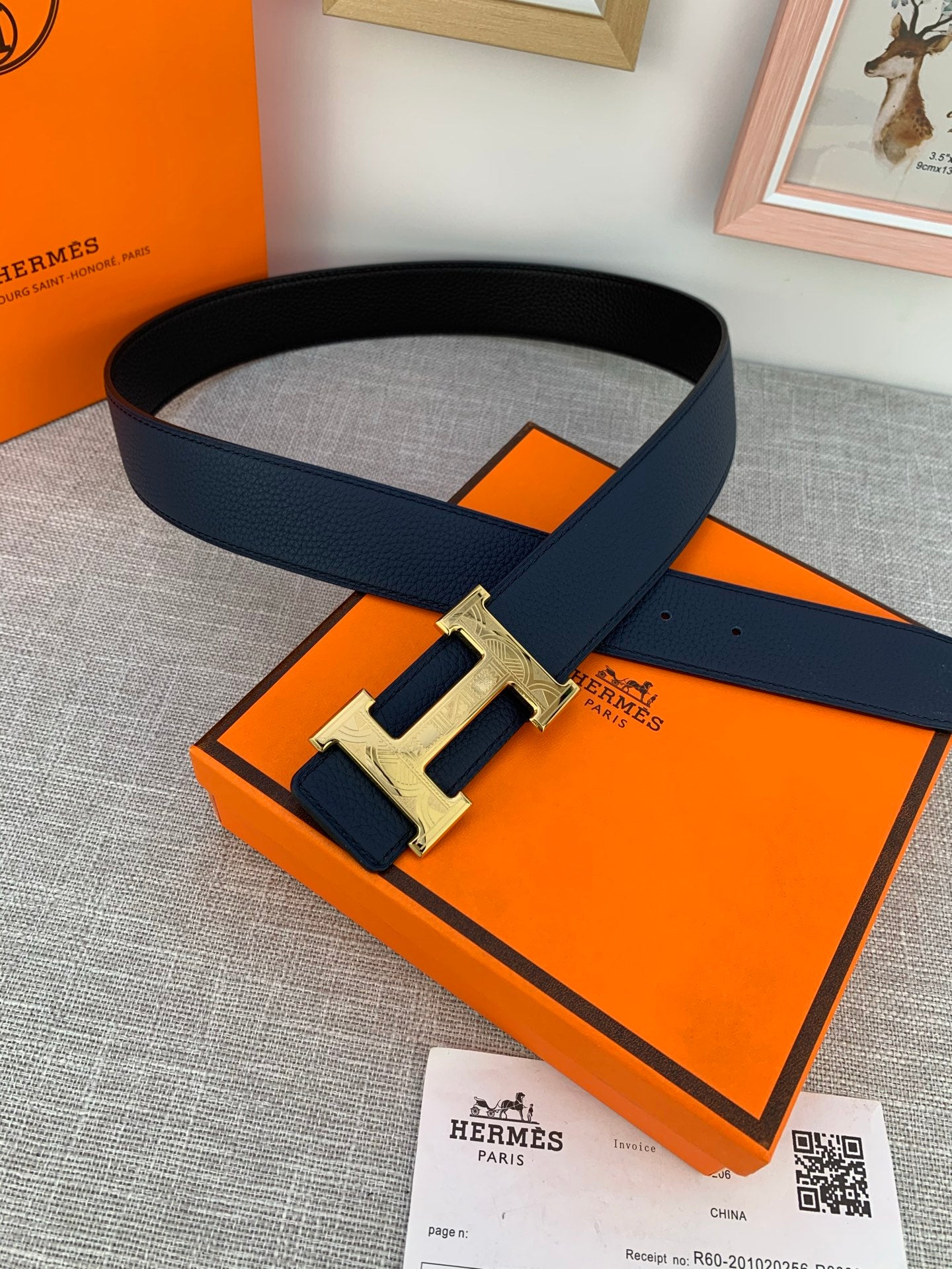 Hermes belt with dark navy strap and gold-tone H buckle, styled on box