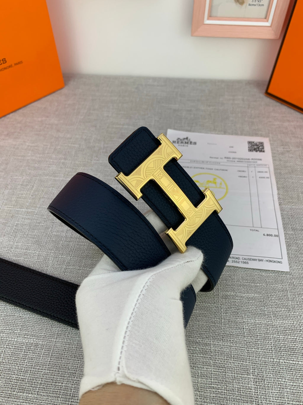 Hermes belt with dark navy strap and silver-tone H buckle, hands holding it