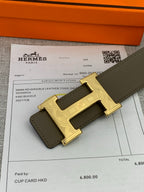 Leather belt close-up showing gold-tone H buckle on olive strap beside receipt.