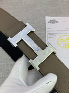 Leather belt close-up with embossed buckle and olive strap, dark underside visible.
