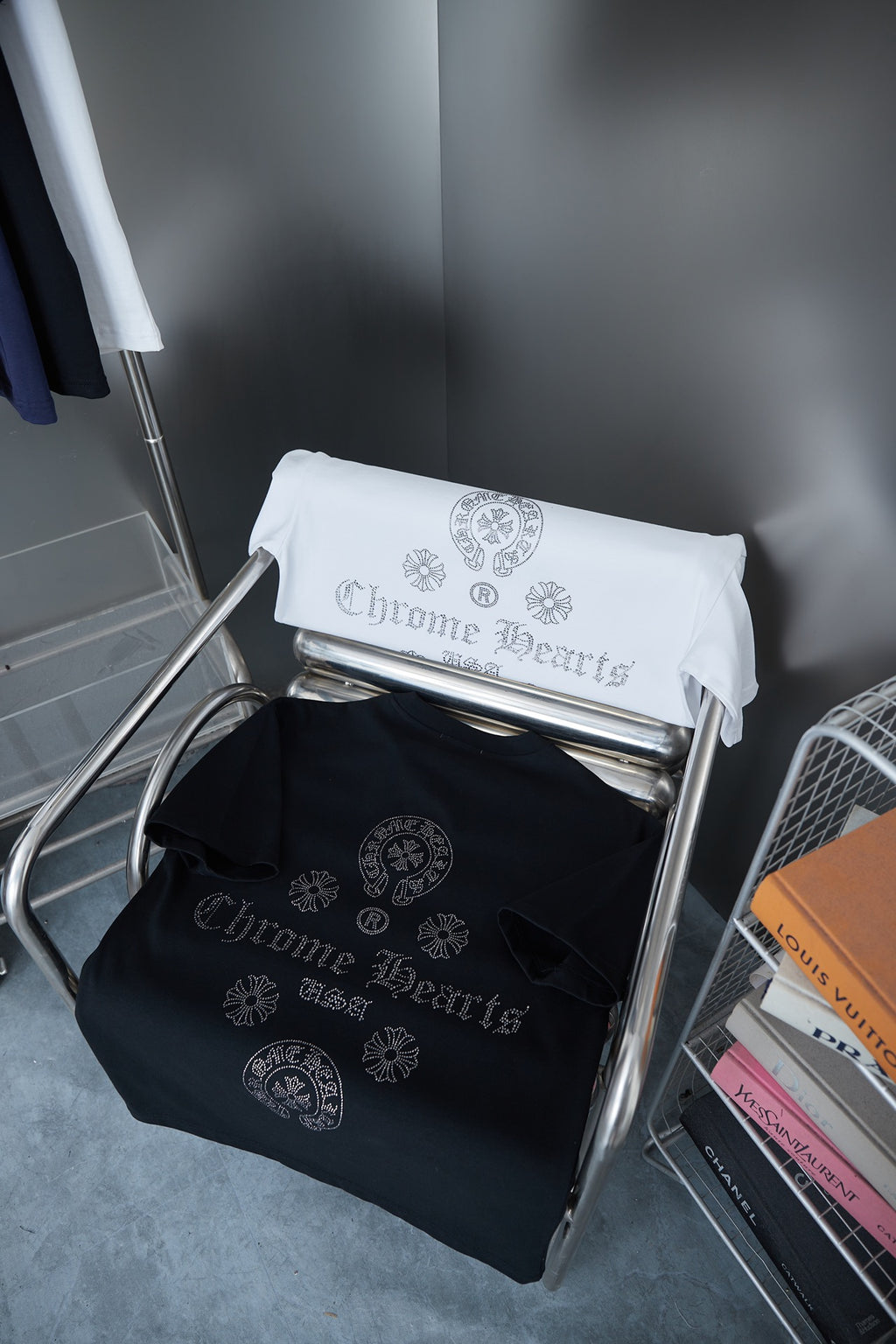 Folded T-shirts on rack: white and dark blue each with rhinestone-style crest