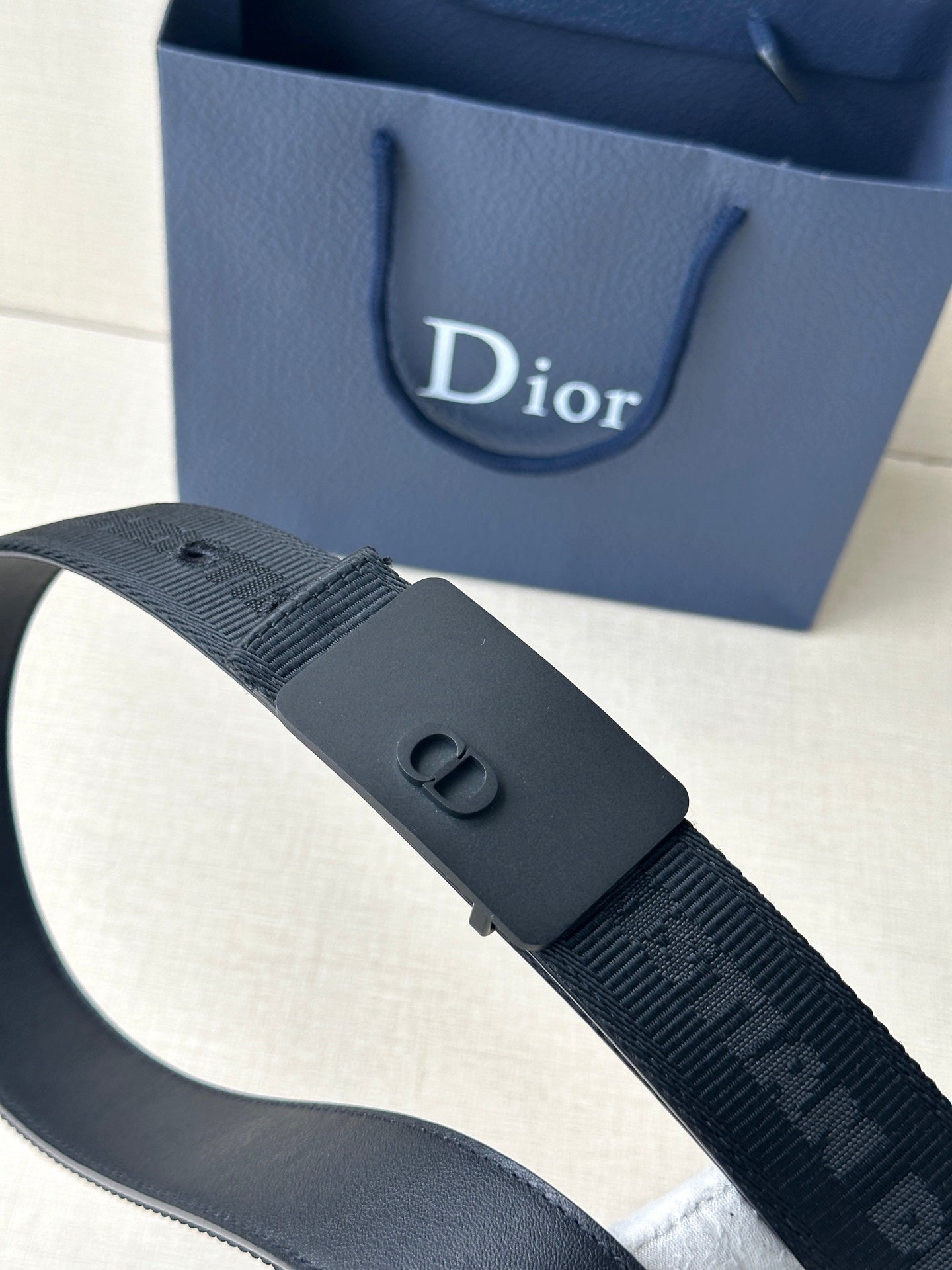 Dior belt buckle detail on dark blue textured strap with embossed pattern