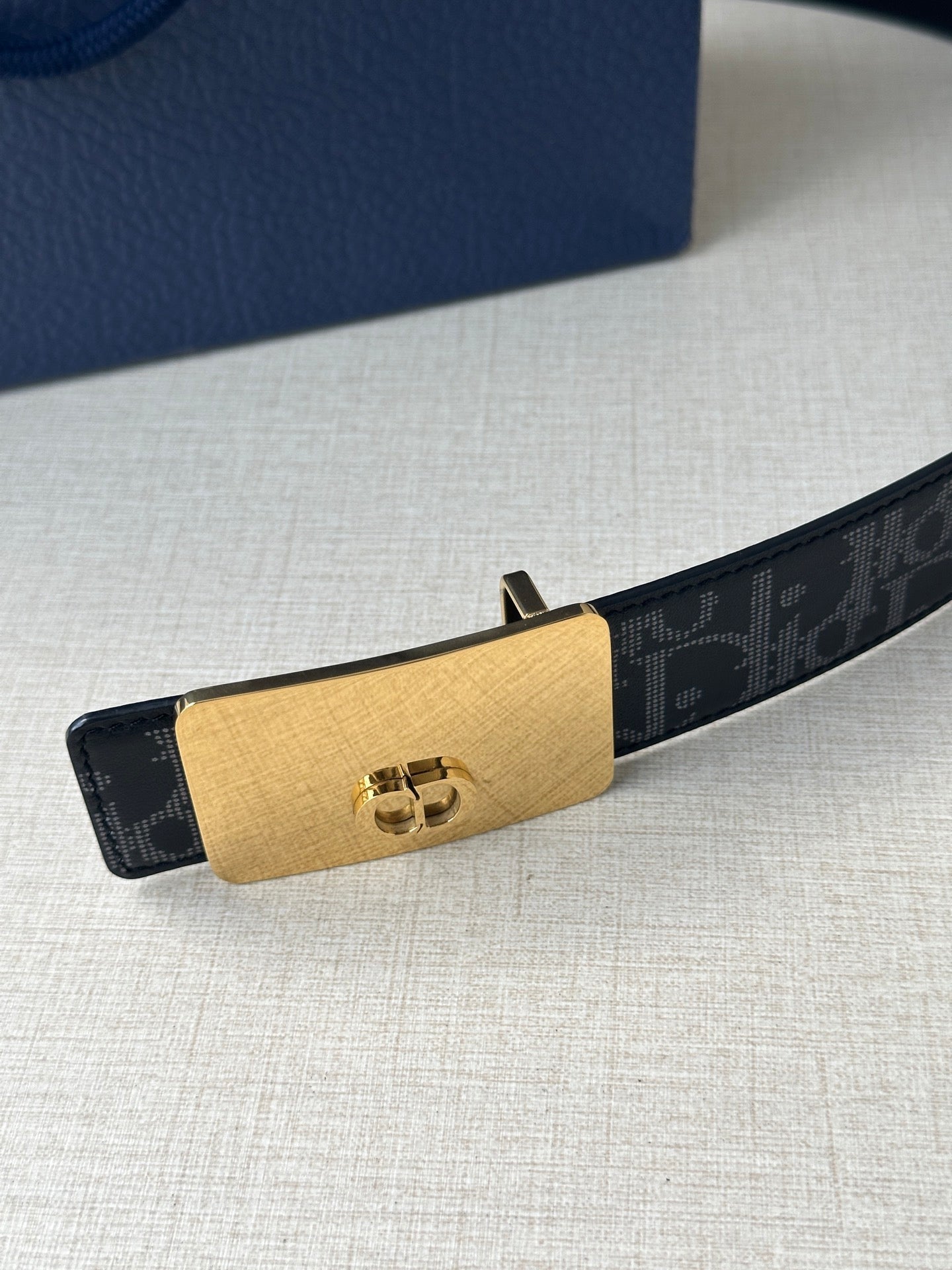 Designer belt with dark monogram strap and gold-tone logo buckle plate
