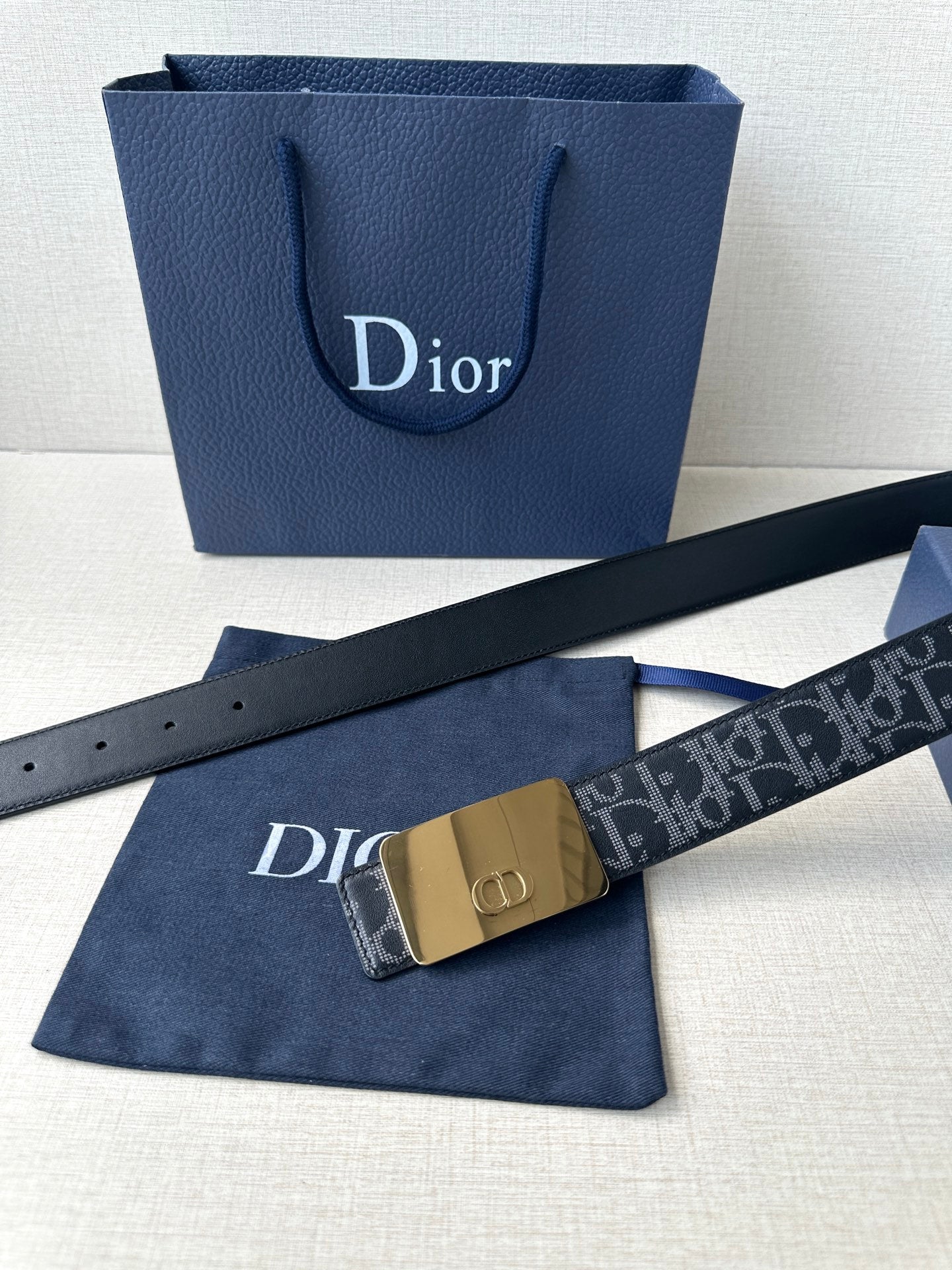 Designer belt with dark strap and gold-tone rectangular buckle with logo