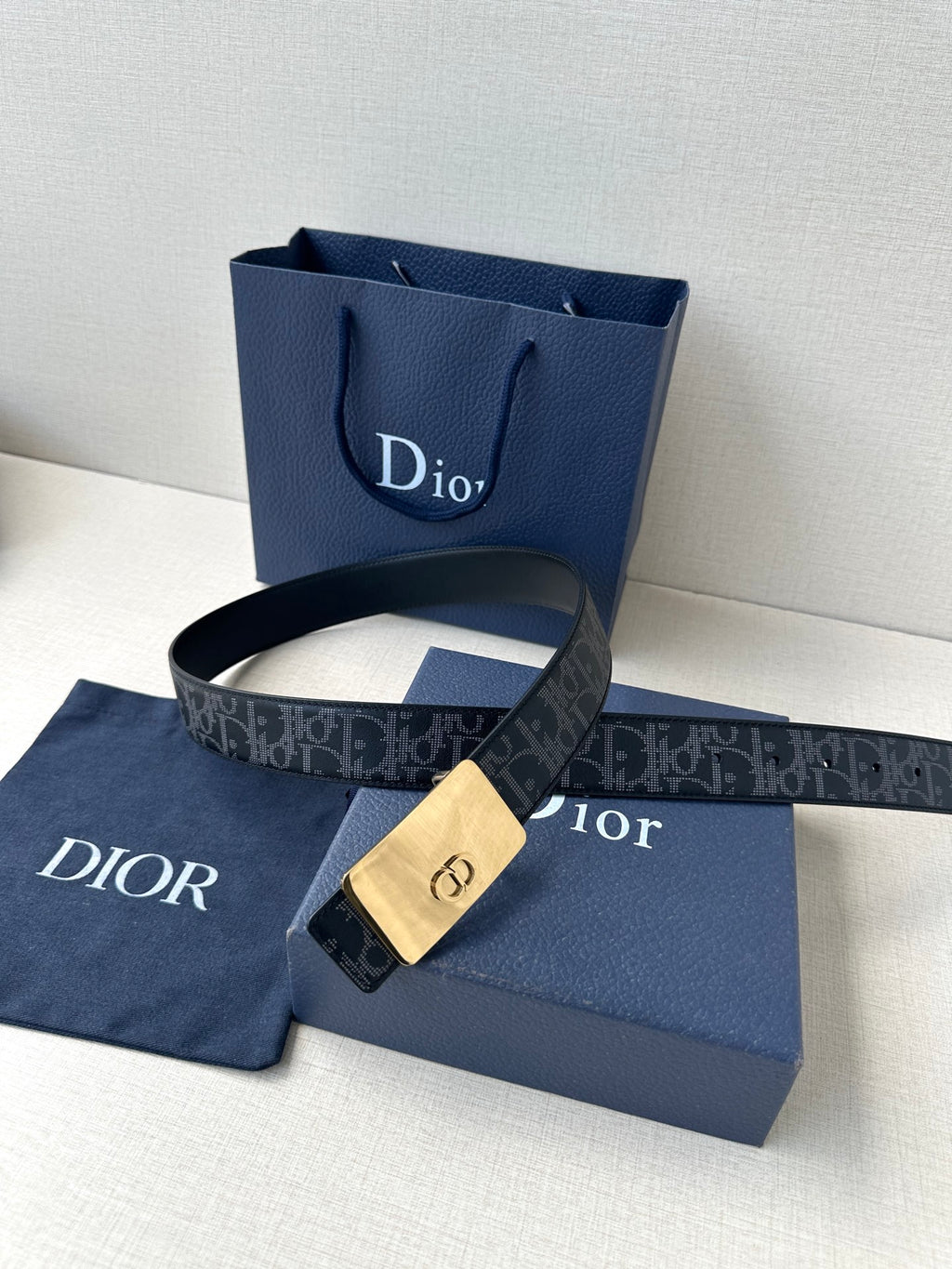 Designer belt with dark monogram strap and gold-tone buckle, flat clasp