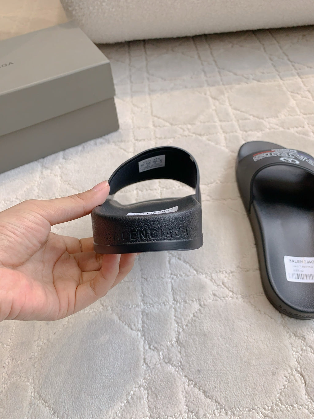 Black Balenciaga slide sandal heel strap with white size label, hand-held view