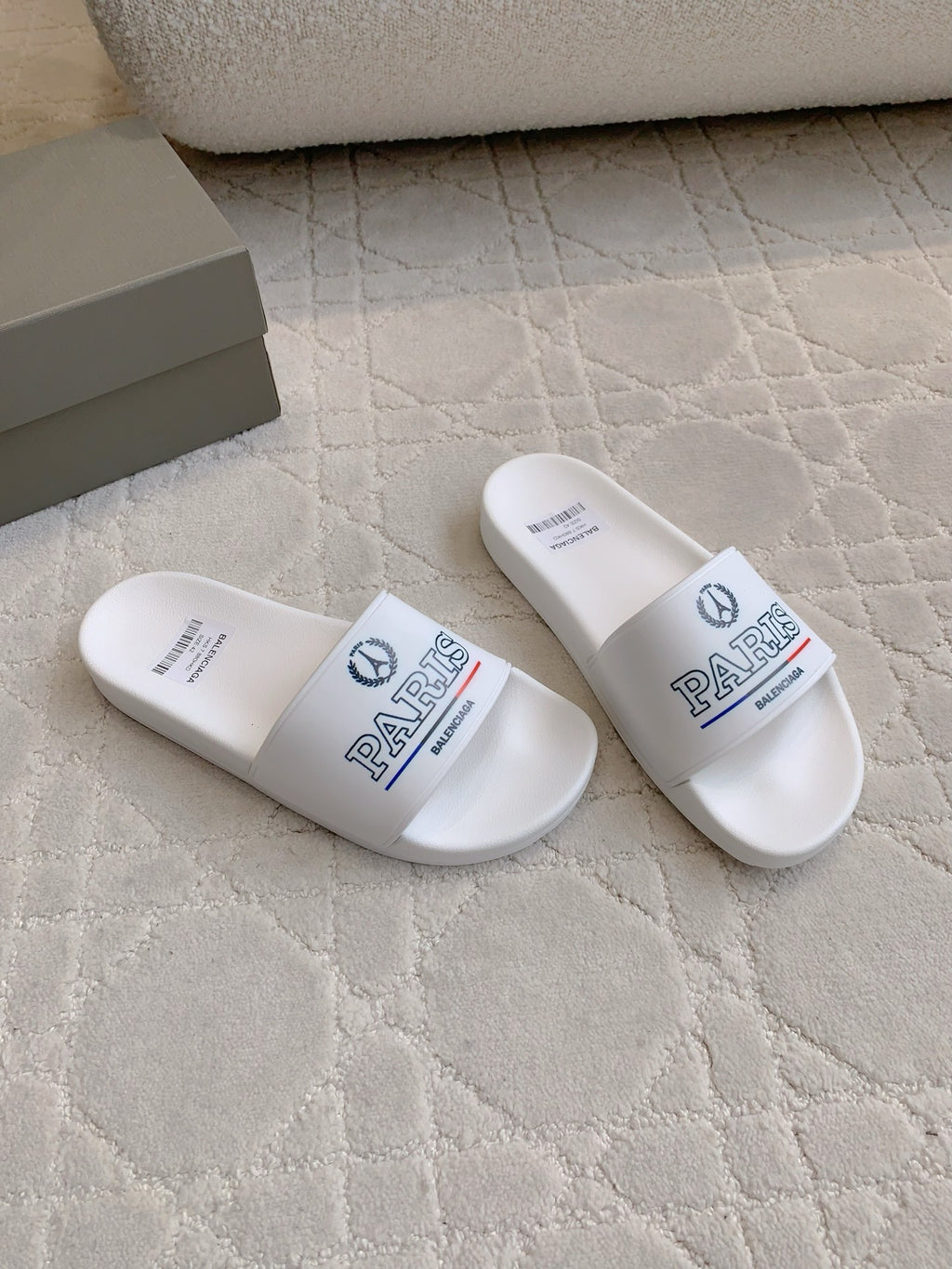 White slide sandals with front straps featuring PARIS text and Balenciaga logo.