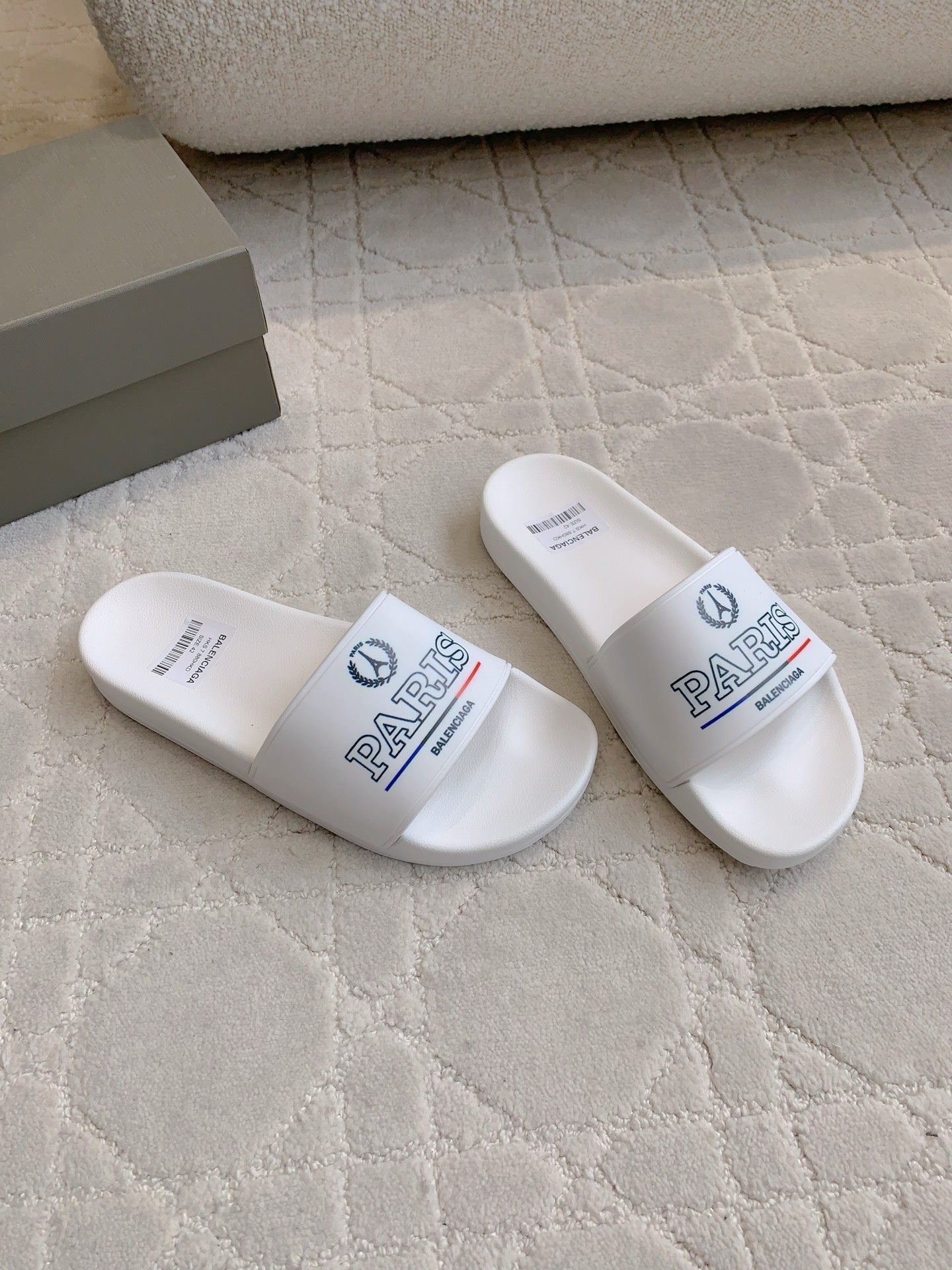 White slide sandals with front straps featuring PARIS text and Balenciaga logo.