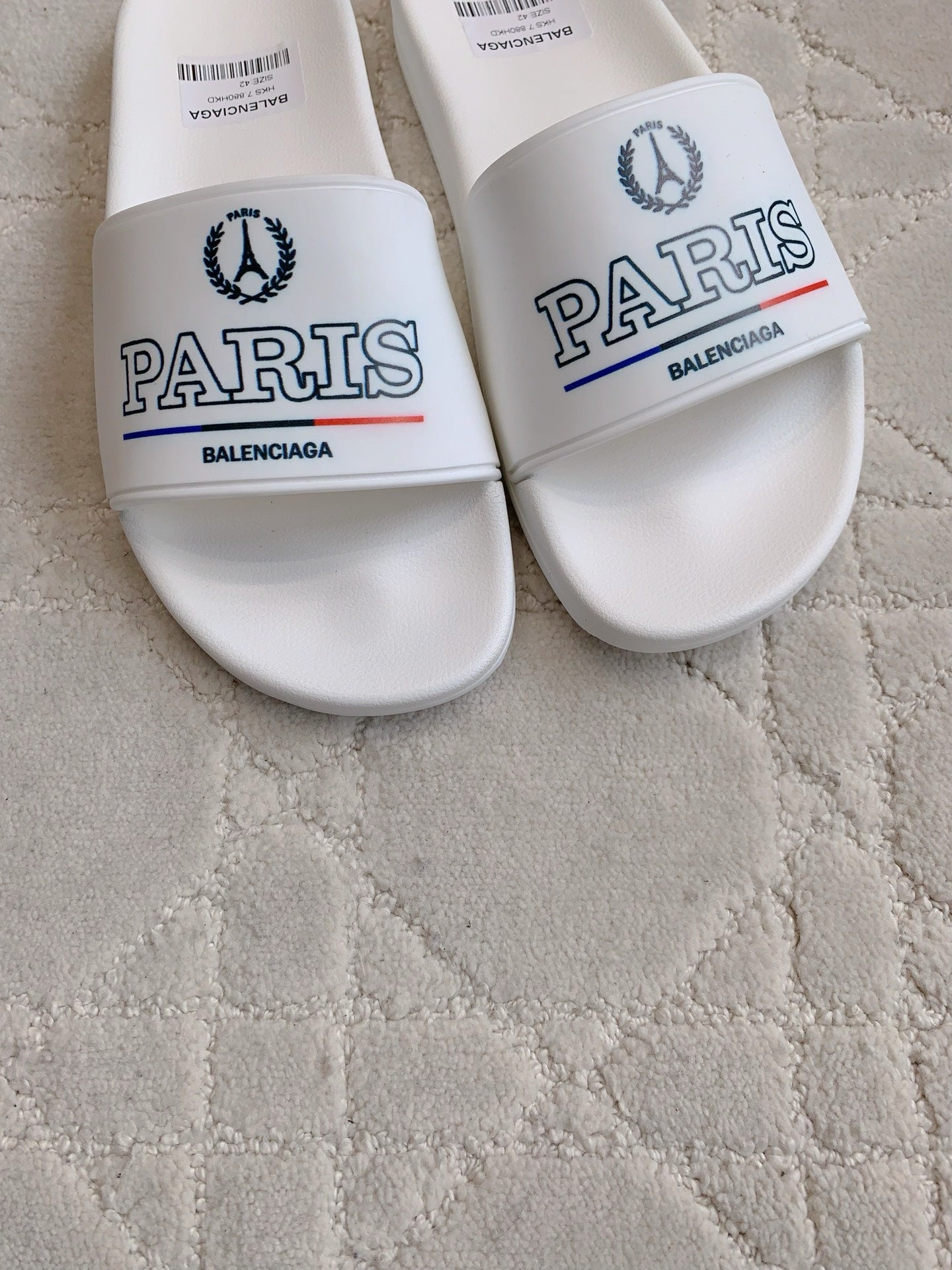 White slide sandals close-up: front straps with PARIS and Balenciaga branding.