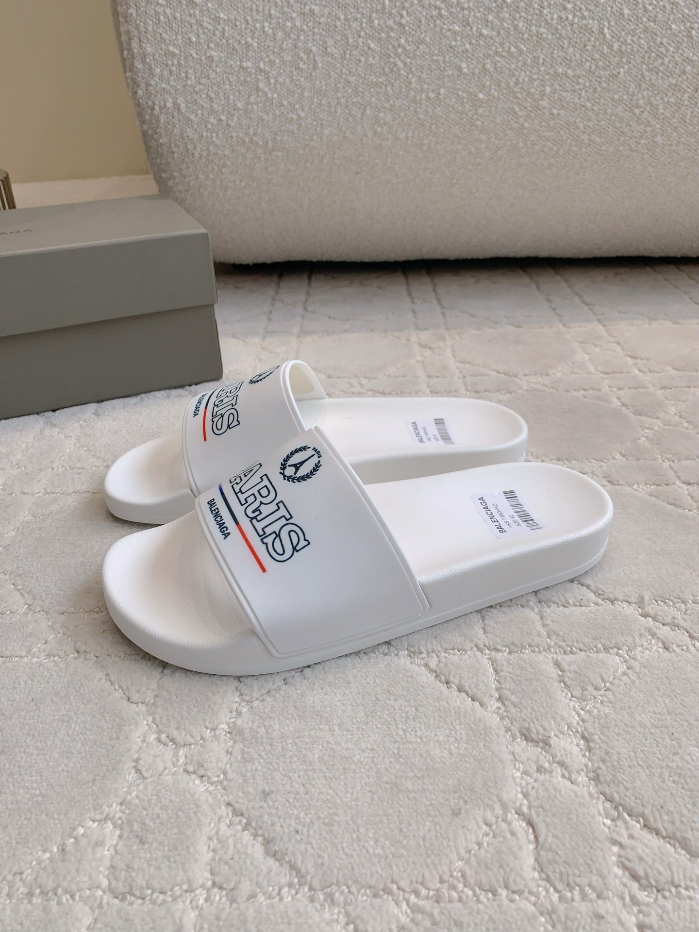 White slide sandals with side strap showing PARIS and Balenciaga branding.