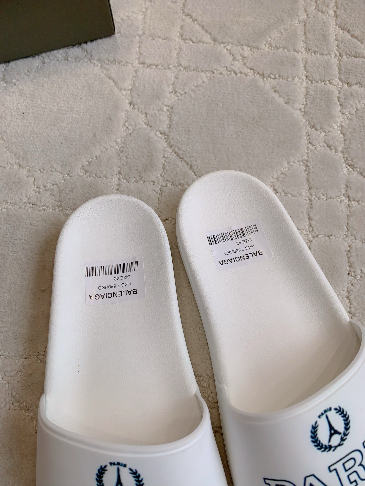 White slide sandals close-up of toe straps with Balenciaga Paris logo detail.