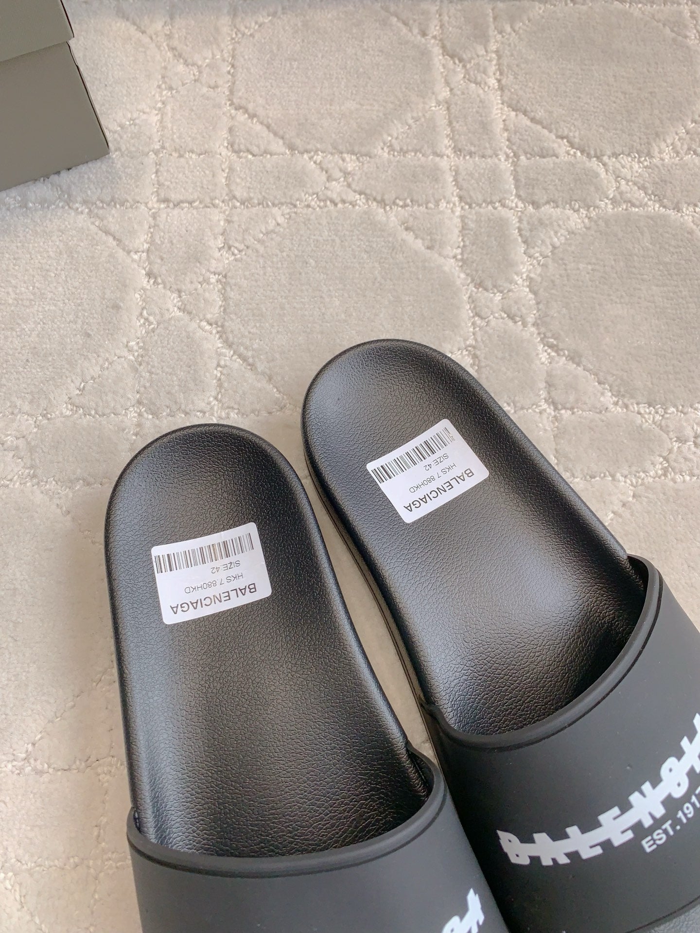 Black slide sandals with curved toe, wide strap, and white label tags