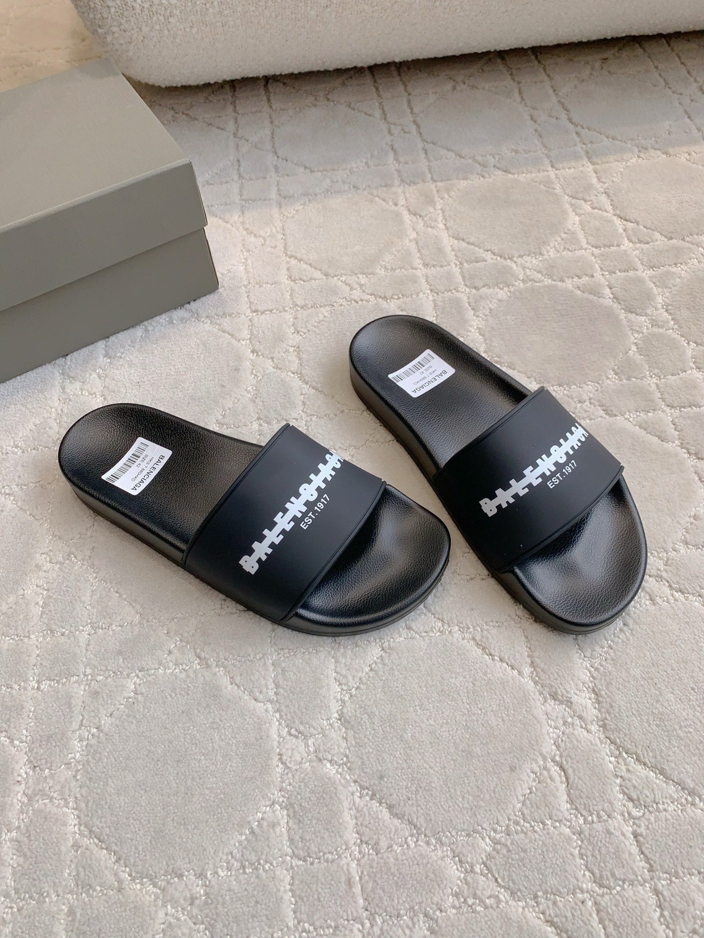 Pair of black slide sandals with wide strap and white logo print on top
