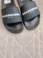 Black slide sandals close-up of wide strap with white logo and EST. 1917 text
