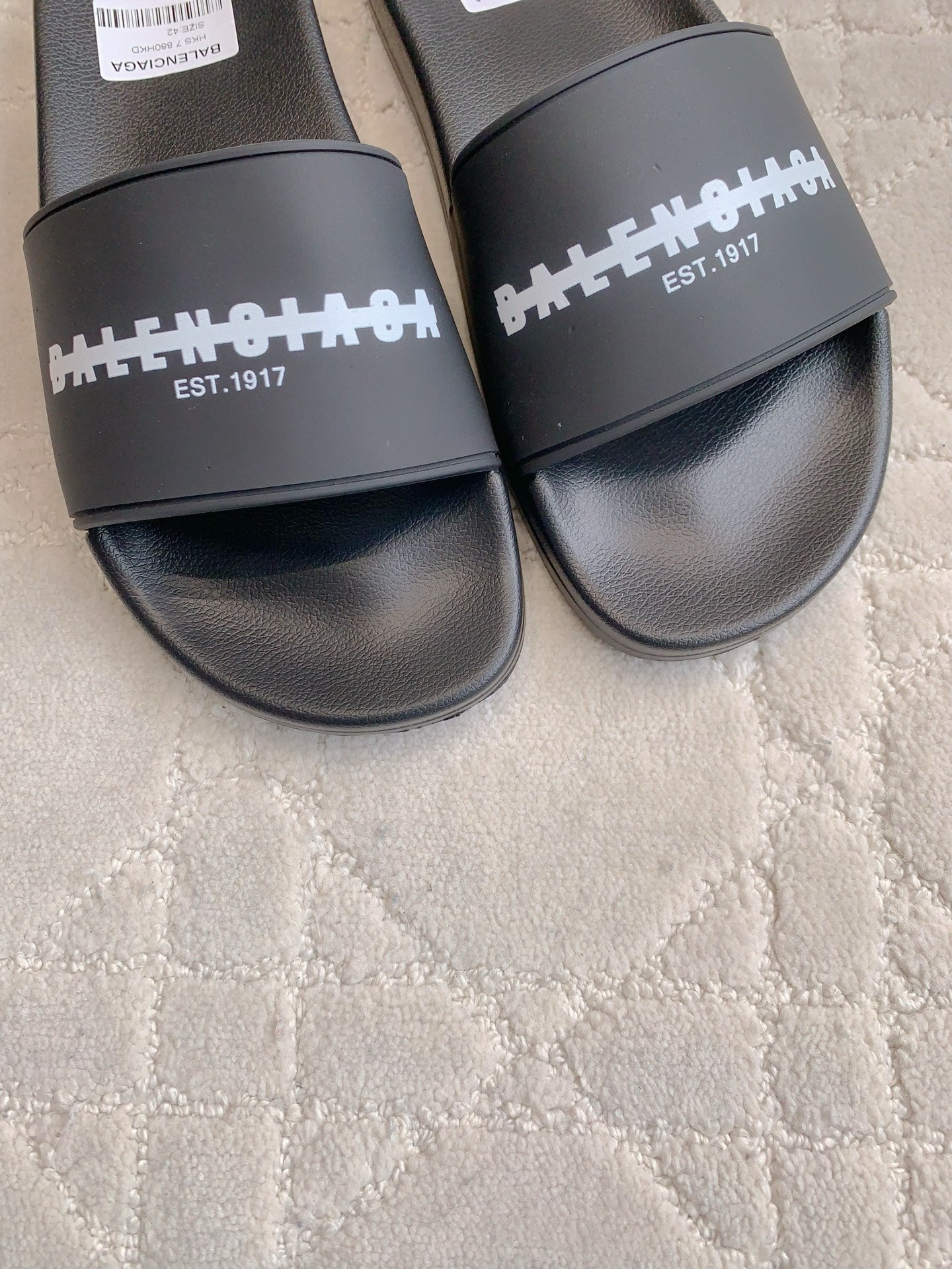 Black slide sandals close-up of wide strap with white logo and EST. 1917 text