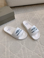 White Balenciaga slide sandals, angled pair with “balenciaga” logo on straps