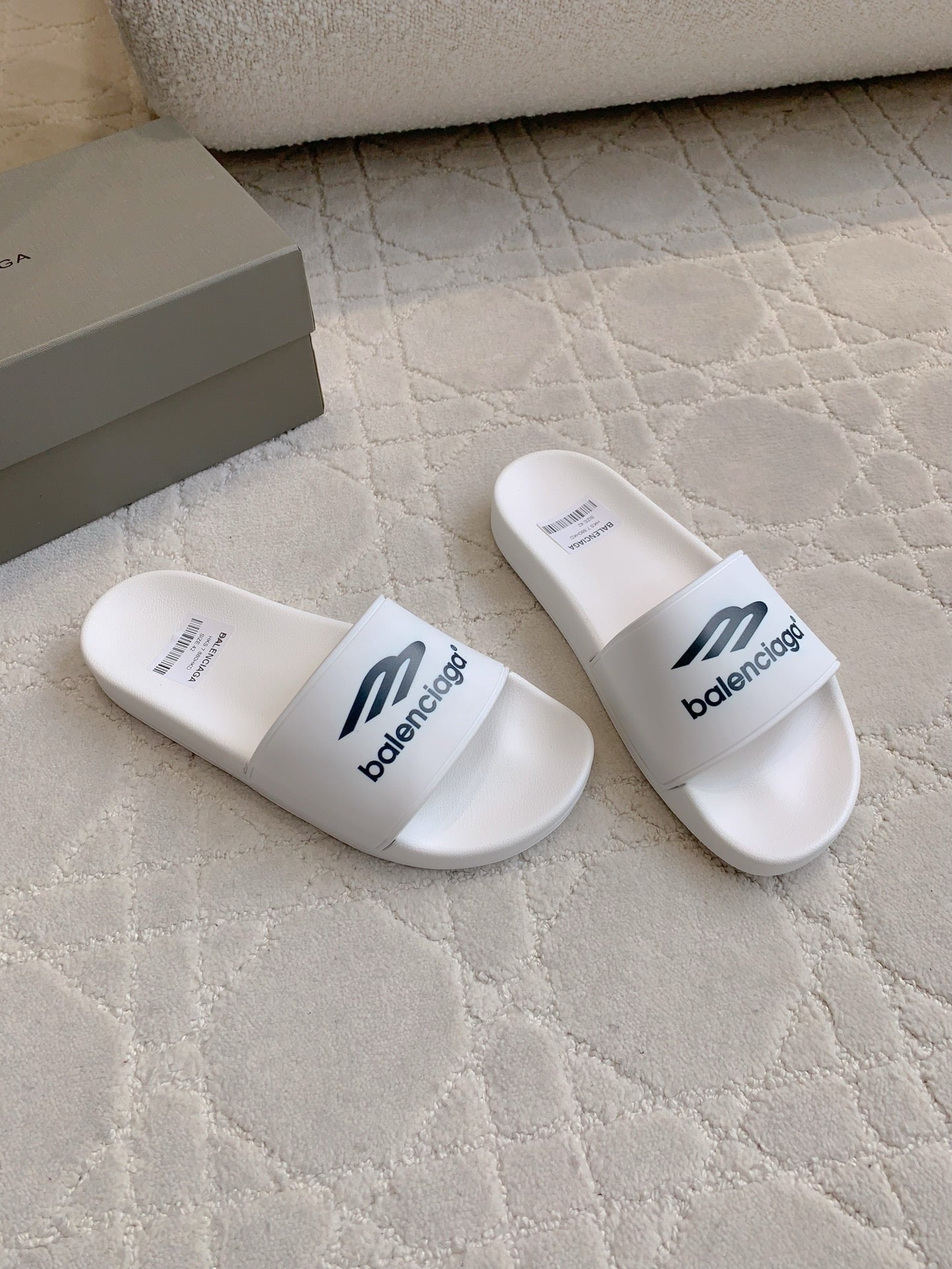 White Balenciaga slide sandals, angled pair with “balenciaga” logo on straps