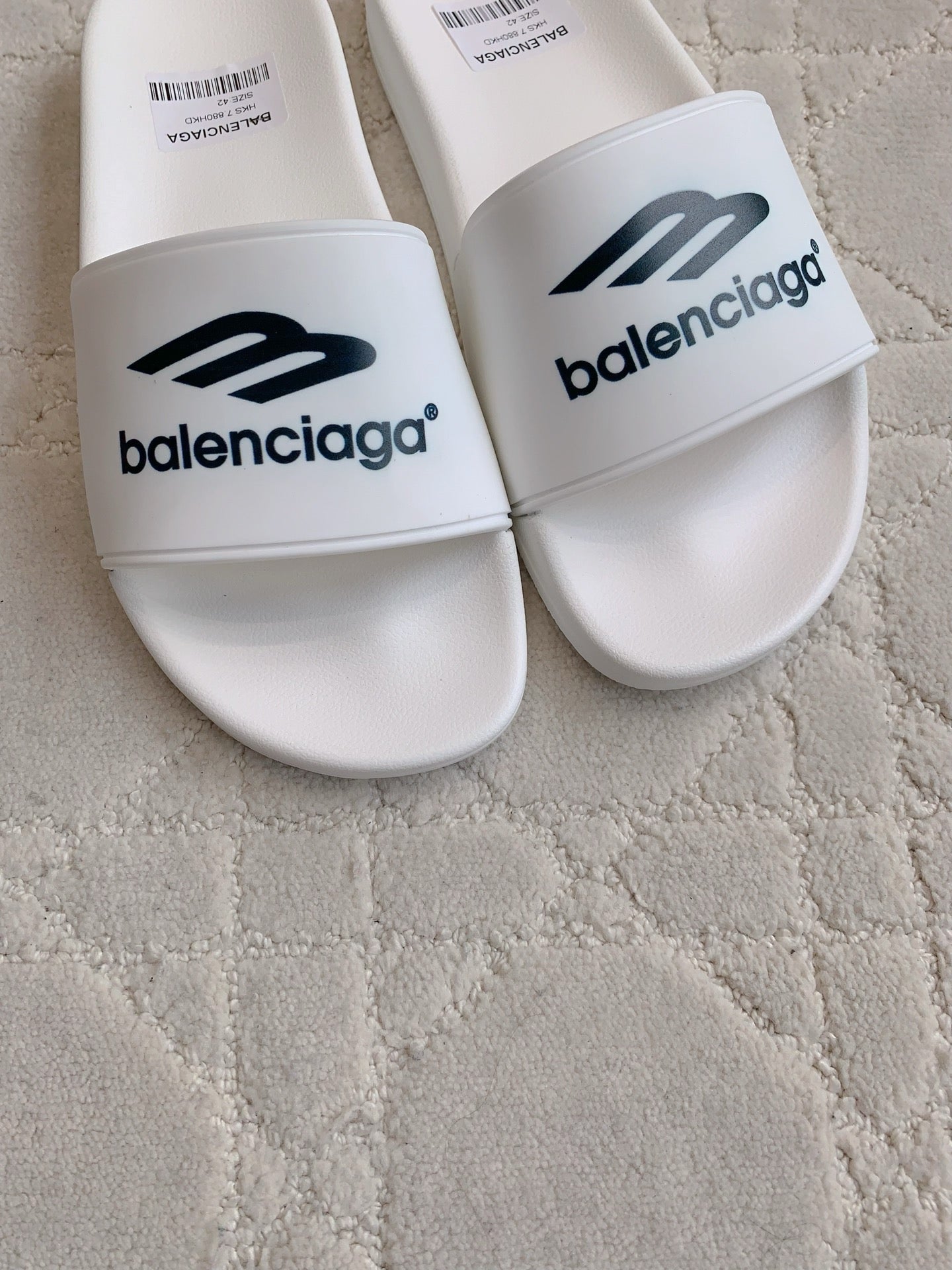 White Balenciaga slide sandals showing wide straps with “balenciaga” logo