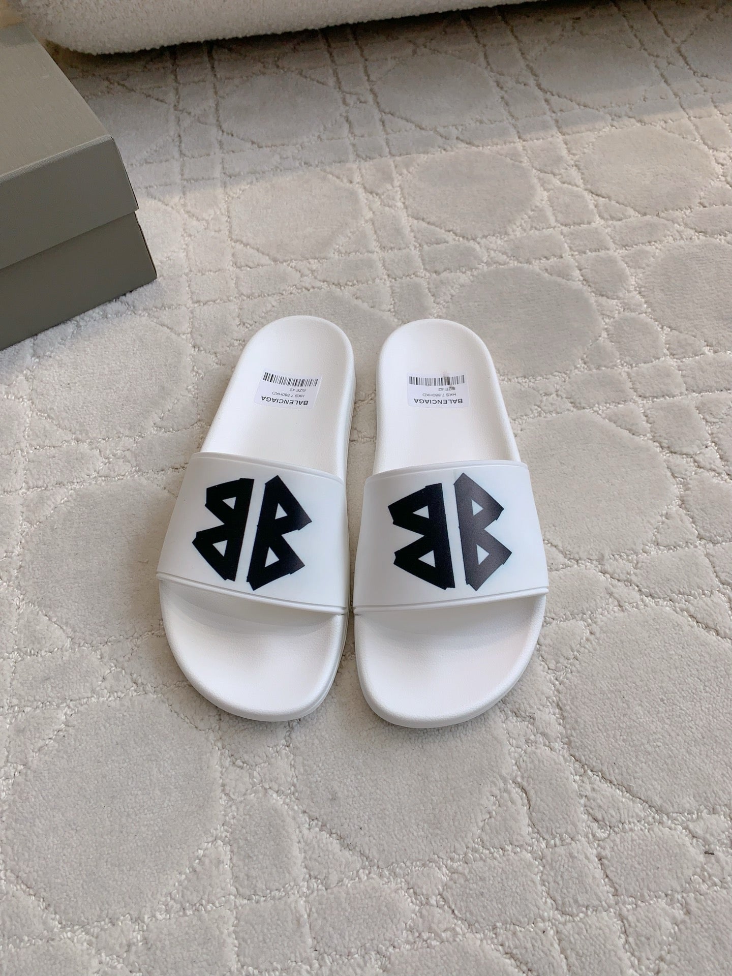 White Balenciaga slide sandals with black logo straps, front view.