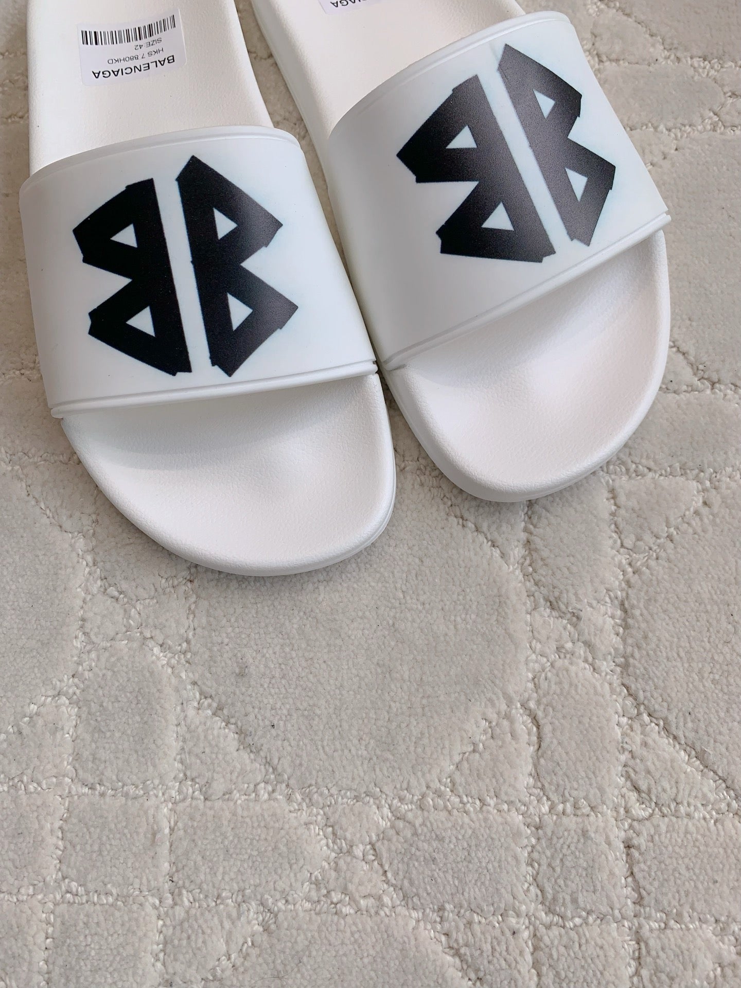White Balenciaga slide sandals with black logo print on front straps.