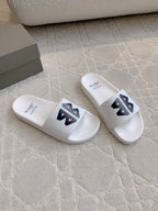 White Balenciaga slide sandals with black logo straps, angled pair view.