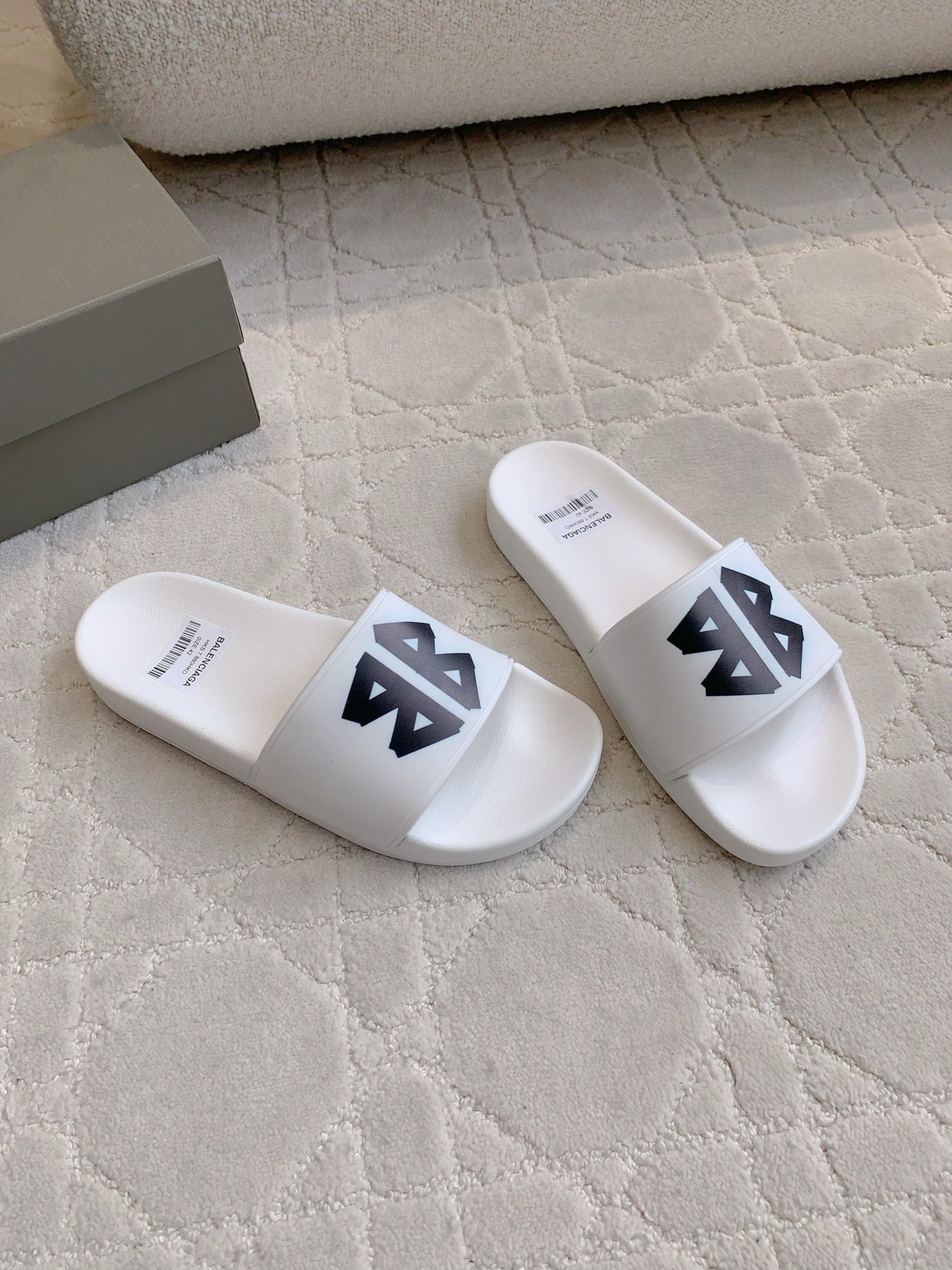 White Balenciaga slide sandals with black logo straps, angled pair view.
