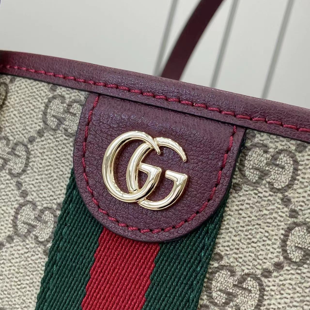 Gucci logo hardware on burgundy leather trim over GG canvas with green-red stripe