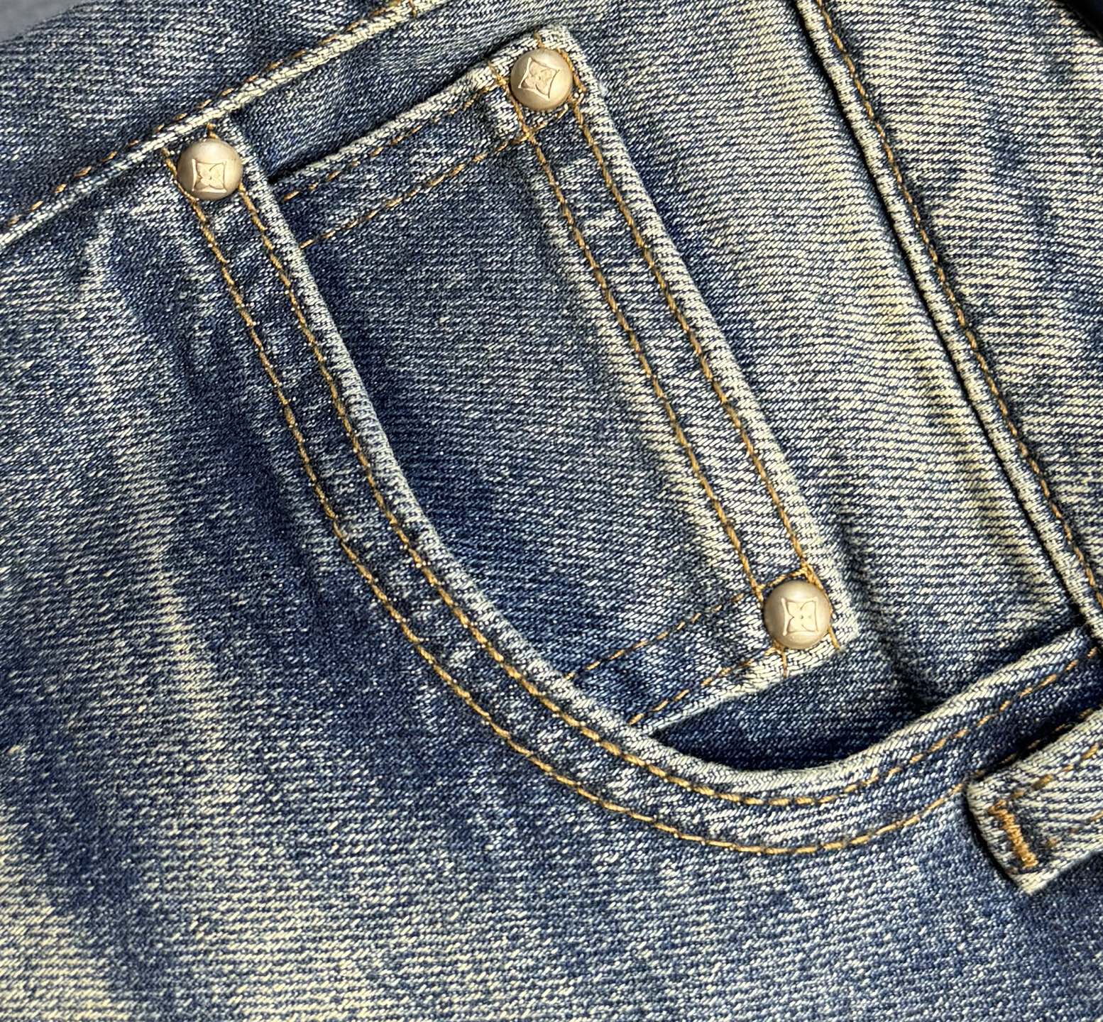 Denim jeans front pocket with gold-toned buttons and curved stitch seam