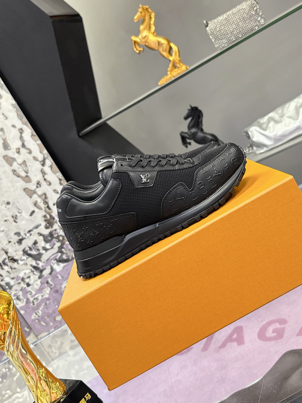 Black low-top Louis Vuitton sneakers on orange box, side view with logo patch.