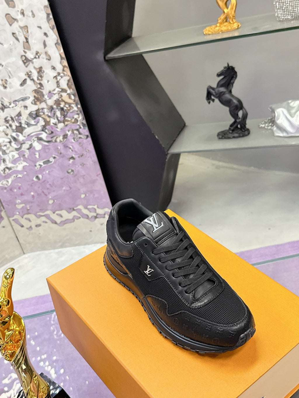 Black lace-up Louis Vuitton sneaker on orange box, side view showing stitching details.