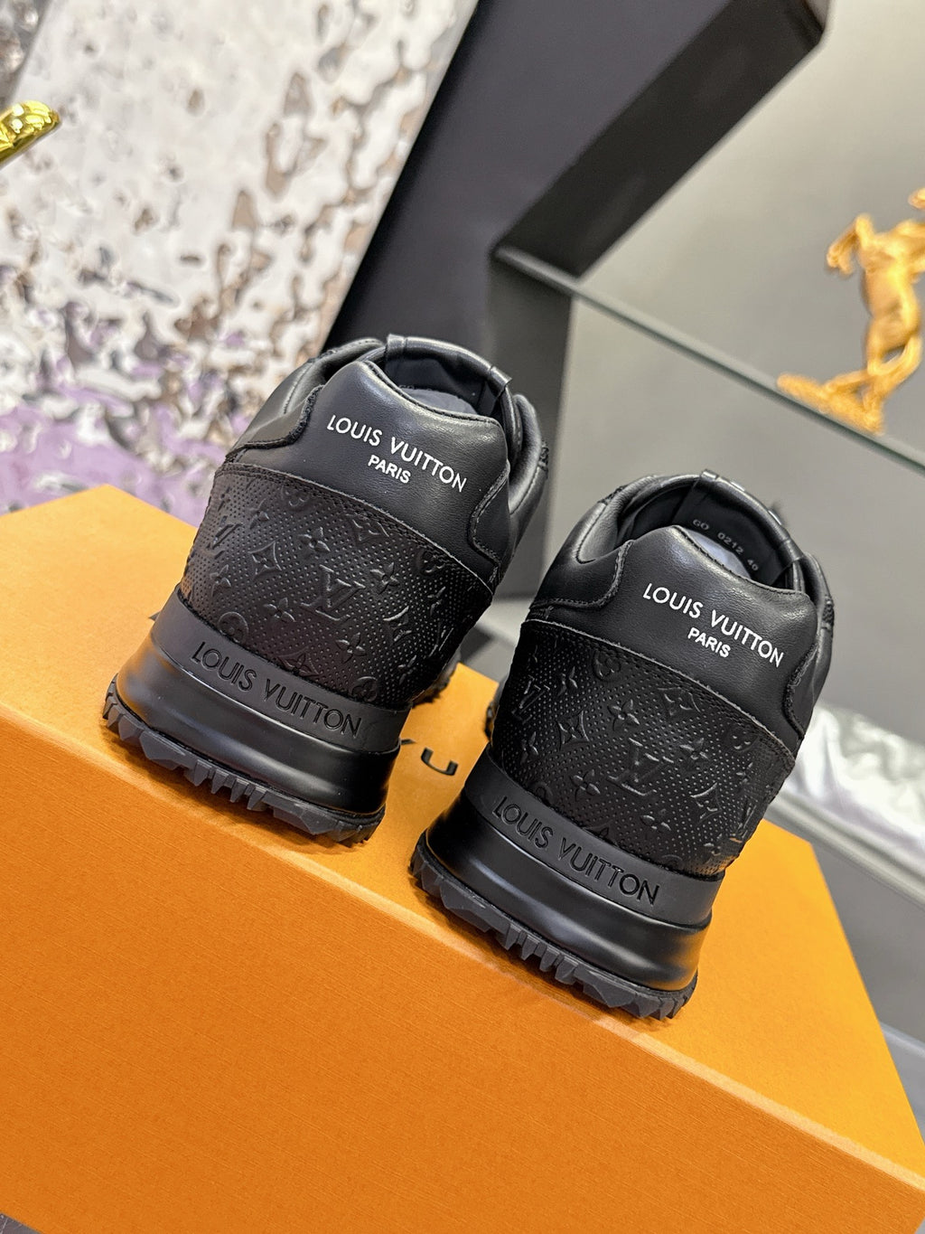 Black Louis Vuitton sneakers on orange box, back view with heel logos and straps.