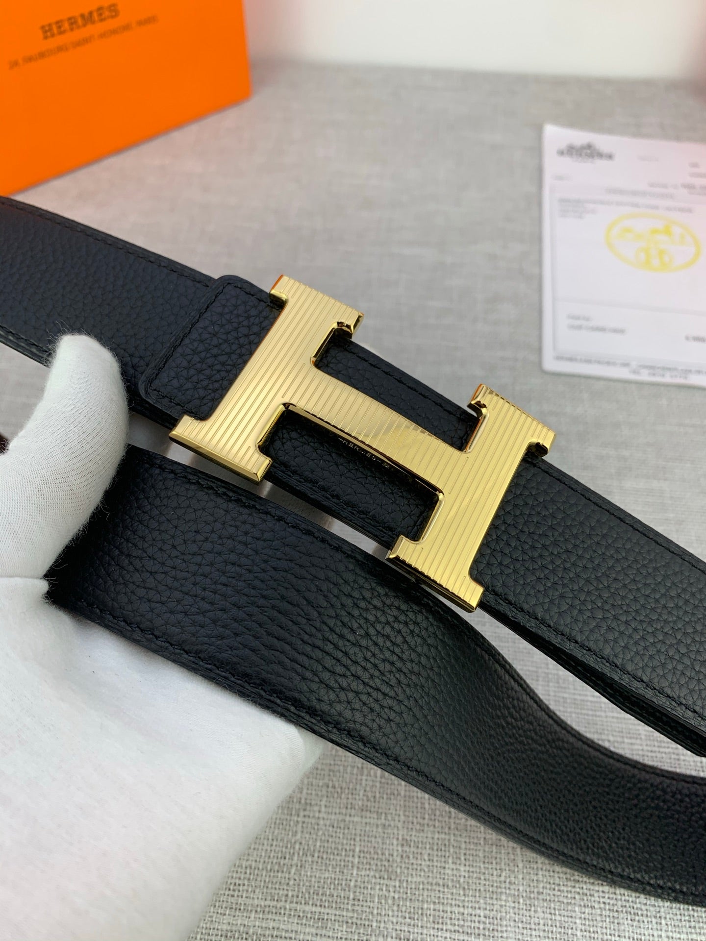 Black leather belt with textured strap and gold-tone H buckle, angled view