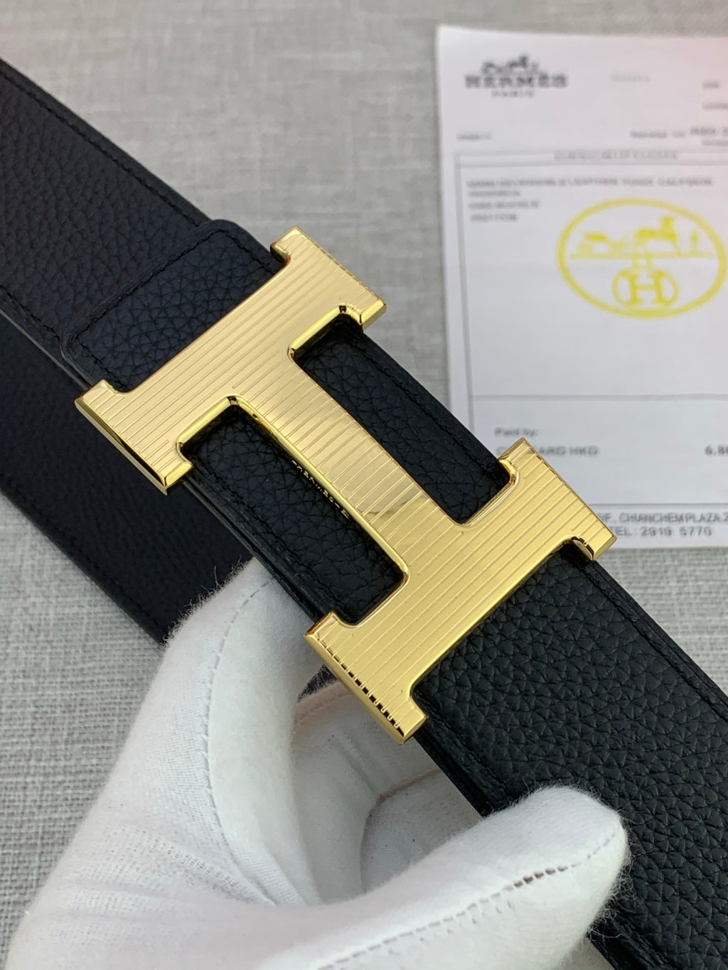 Close-up of black leather belt with textured strap and gold-tone H buckle