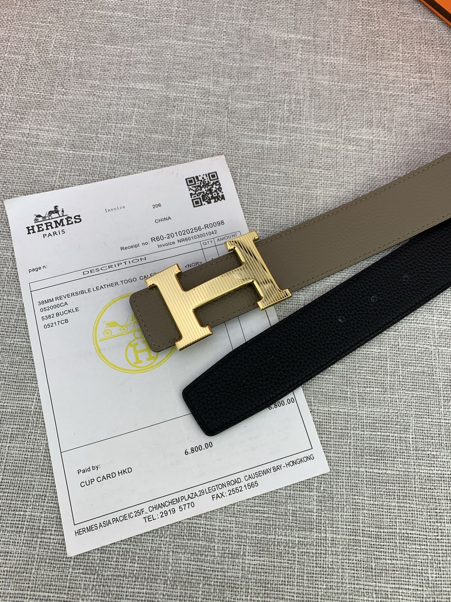 Close-up of reversible belt buckle: gold-tone H on dark strap; certification card below.