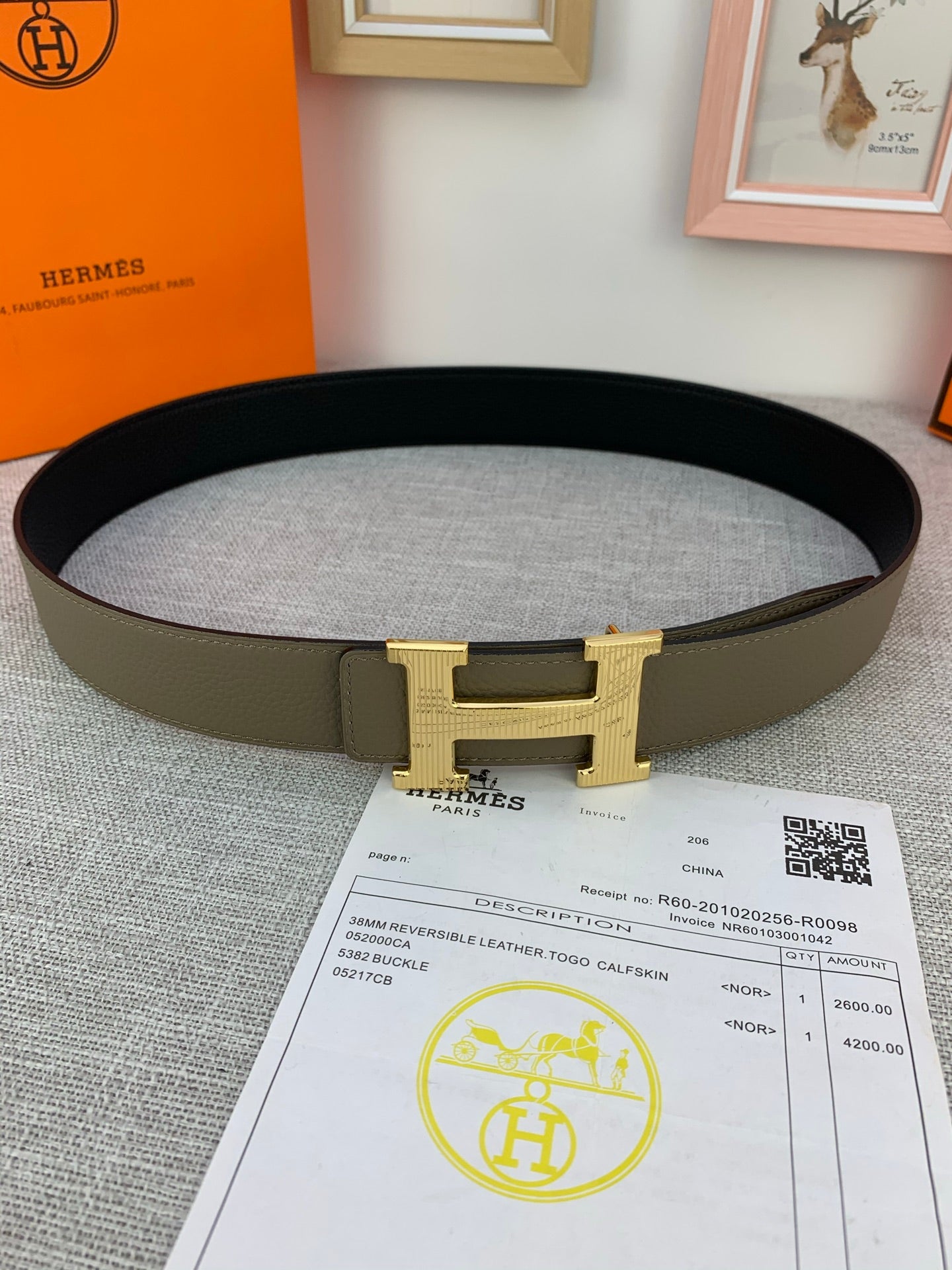 Reversible leather belt, flat lay: dark olive strap with gold-tone H buckle and black underside.
