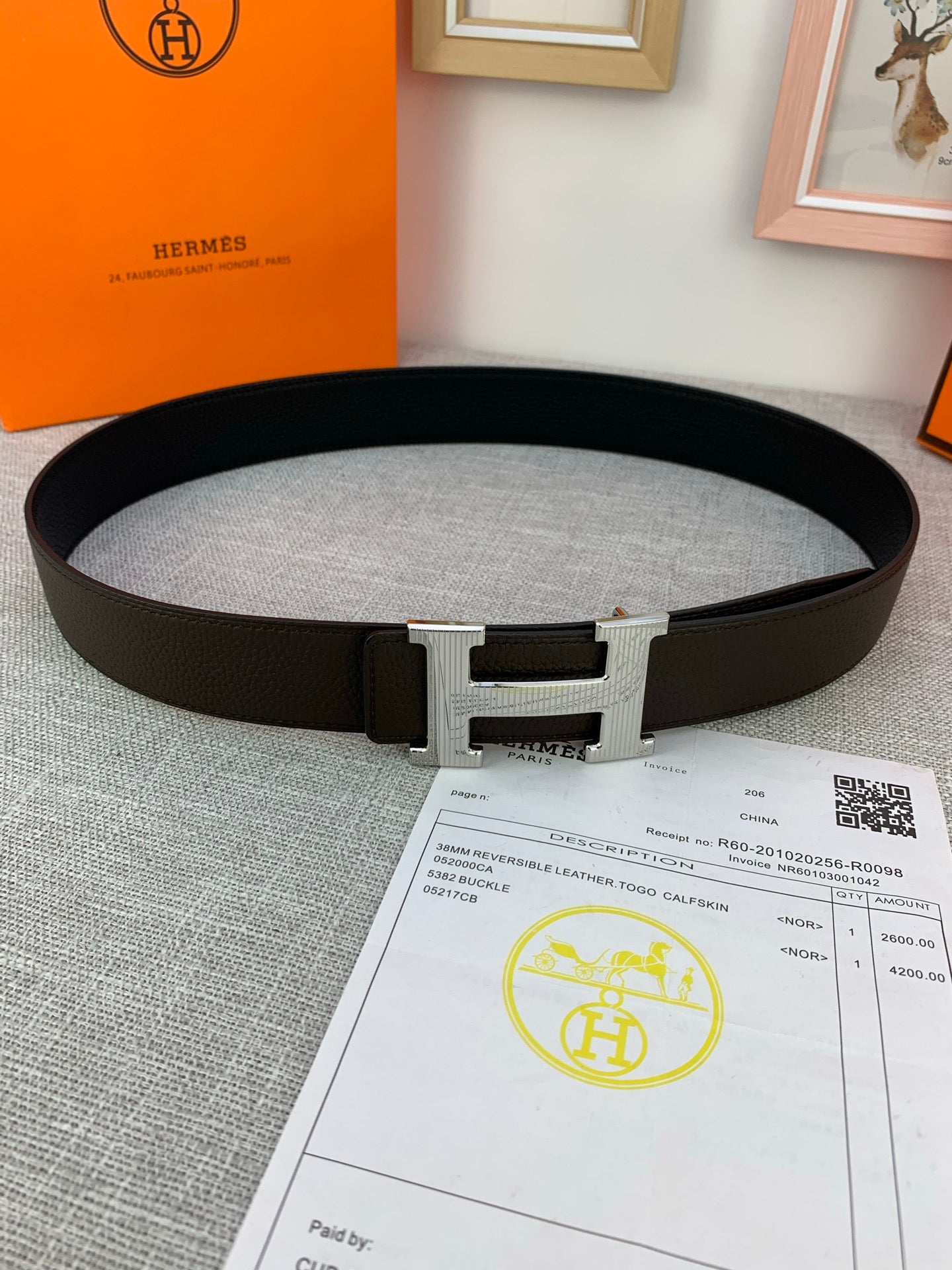 Hermes belt dark leather with silver-toned buckle clasp on light gray surface