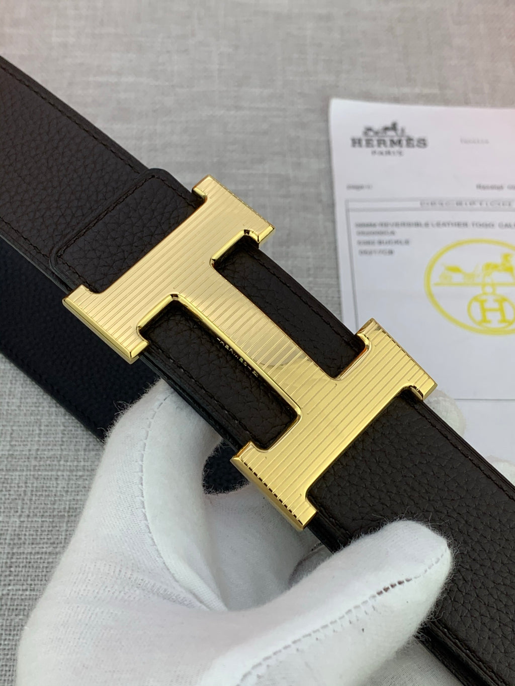 Hermes belt close-up of gold-toned H buckle on dark textured leather strap