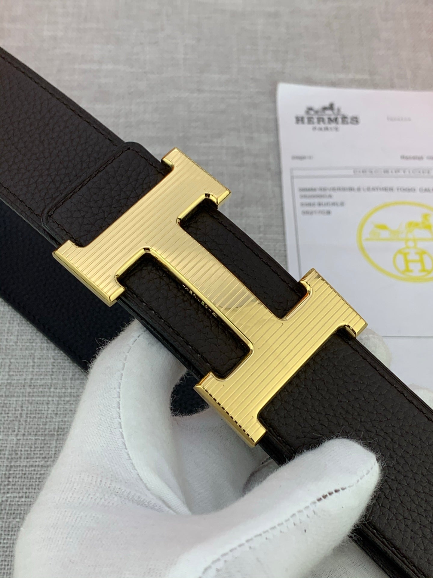 Hermes belt close-up of gold-toned H buckle on dark textured leather strap