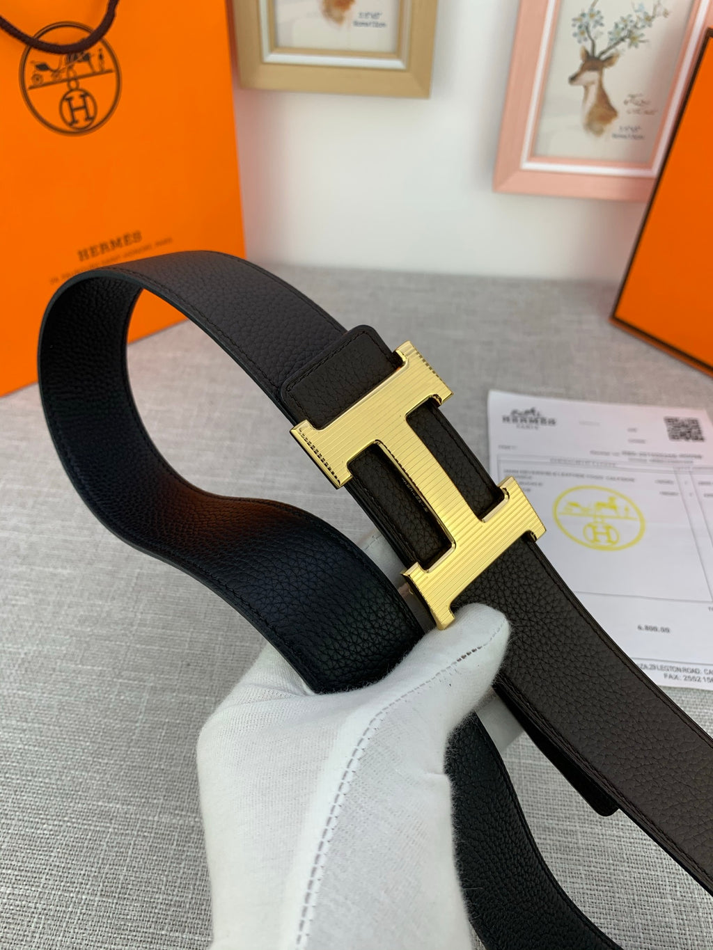 Hermes belt dark leather strap with gold-toned H buckle, laid across papers